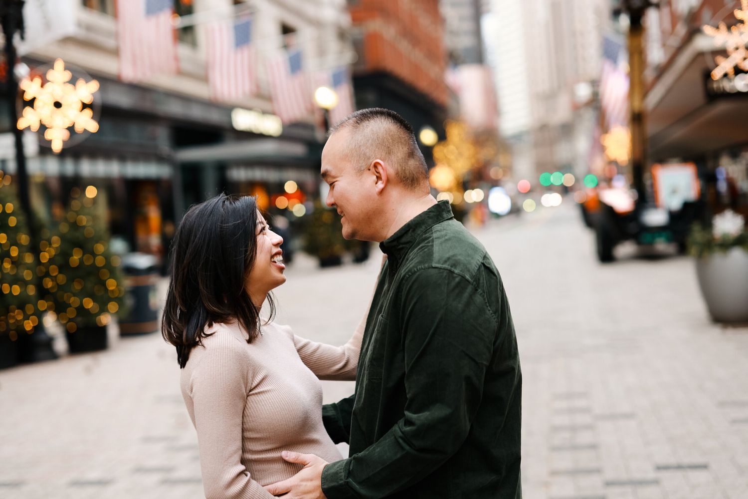Couple sharing a romantic moment on a city street decorated with twinkling holiday lights.