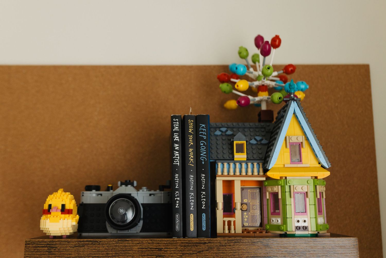 Decorative shelf display with colorful toy houses, books, and balloons against a neutral wall.