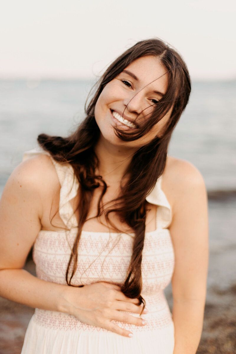 Woman in white dress laughing joyfully during a beach photoshoot at sunset.