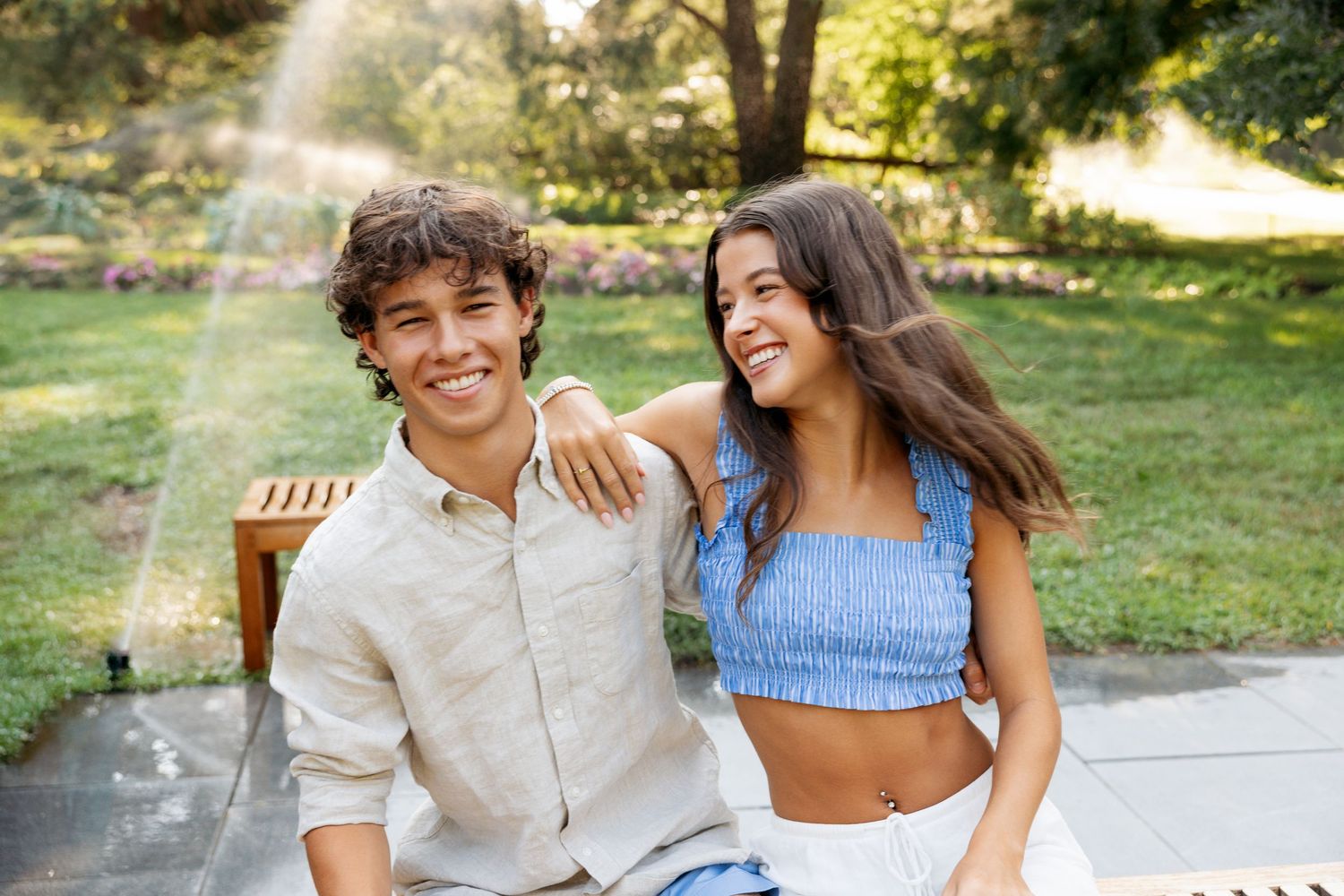 Two people share intimate smiles while sitting outdoors in summer attire.