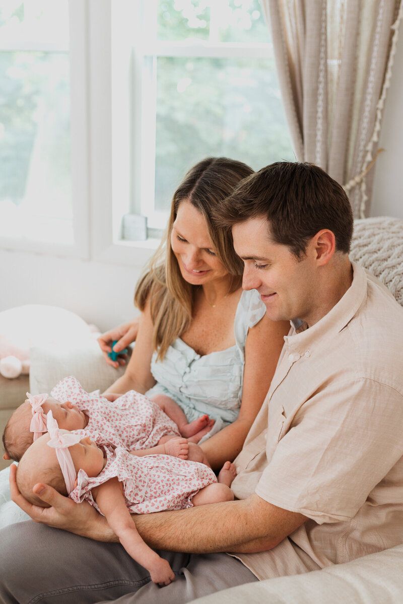Family shares intimate moment on grey couch by bright windows.