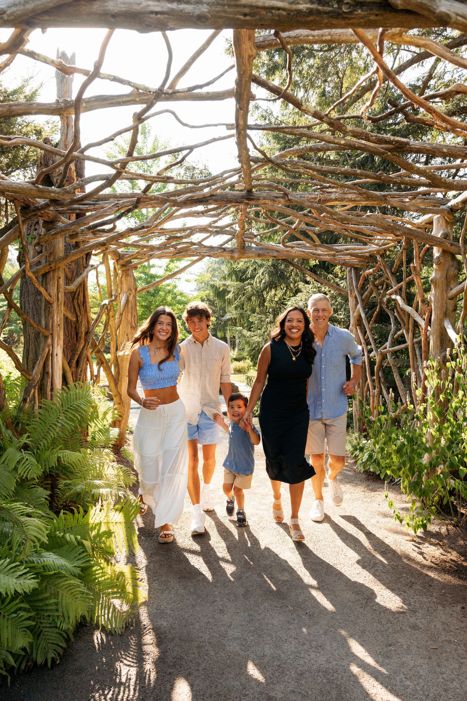 Group walking through a rustic wooden arbor pathway lined with tropical plants.