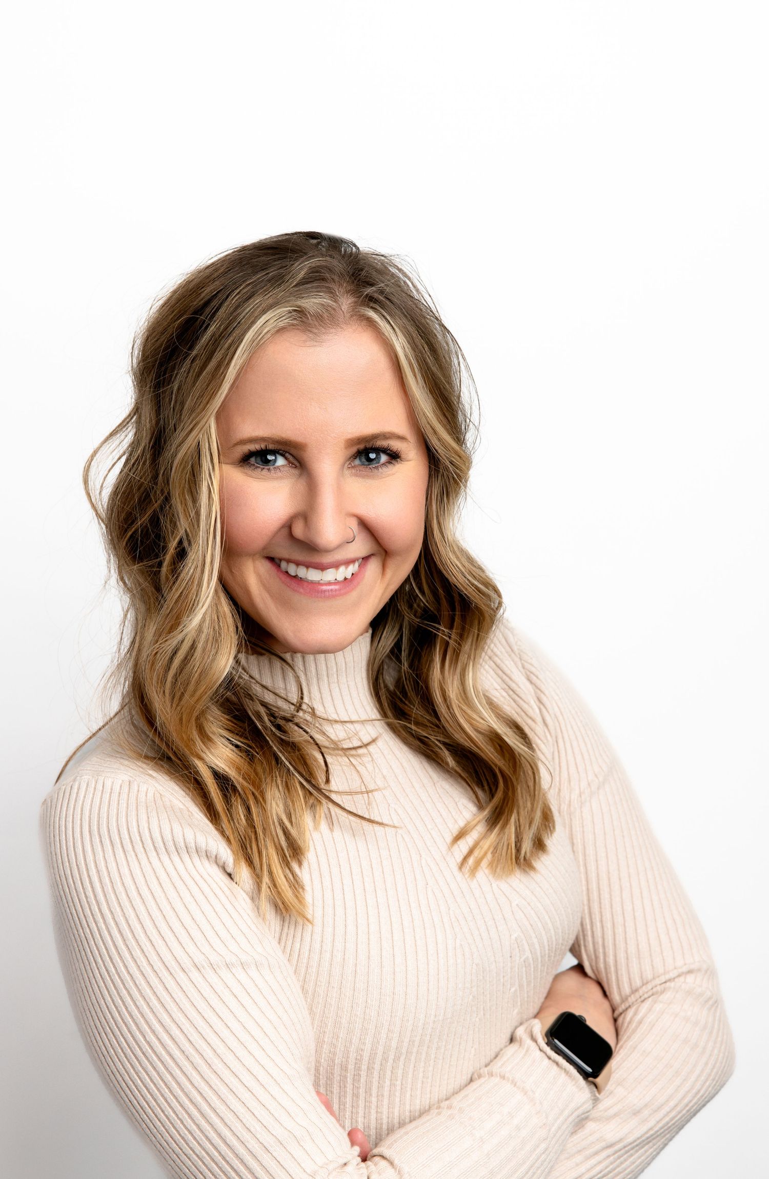 Smiling blonde woman in cream turtleneck sweater with arms crossed, professional headshot on white background.