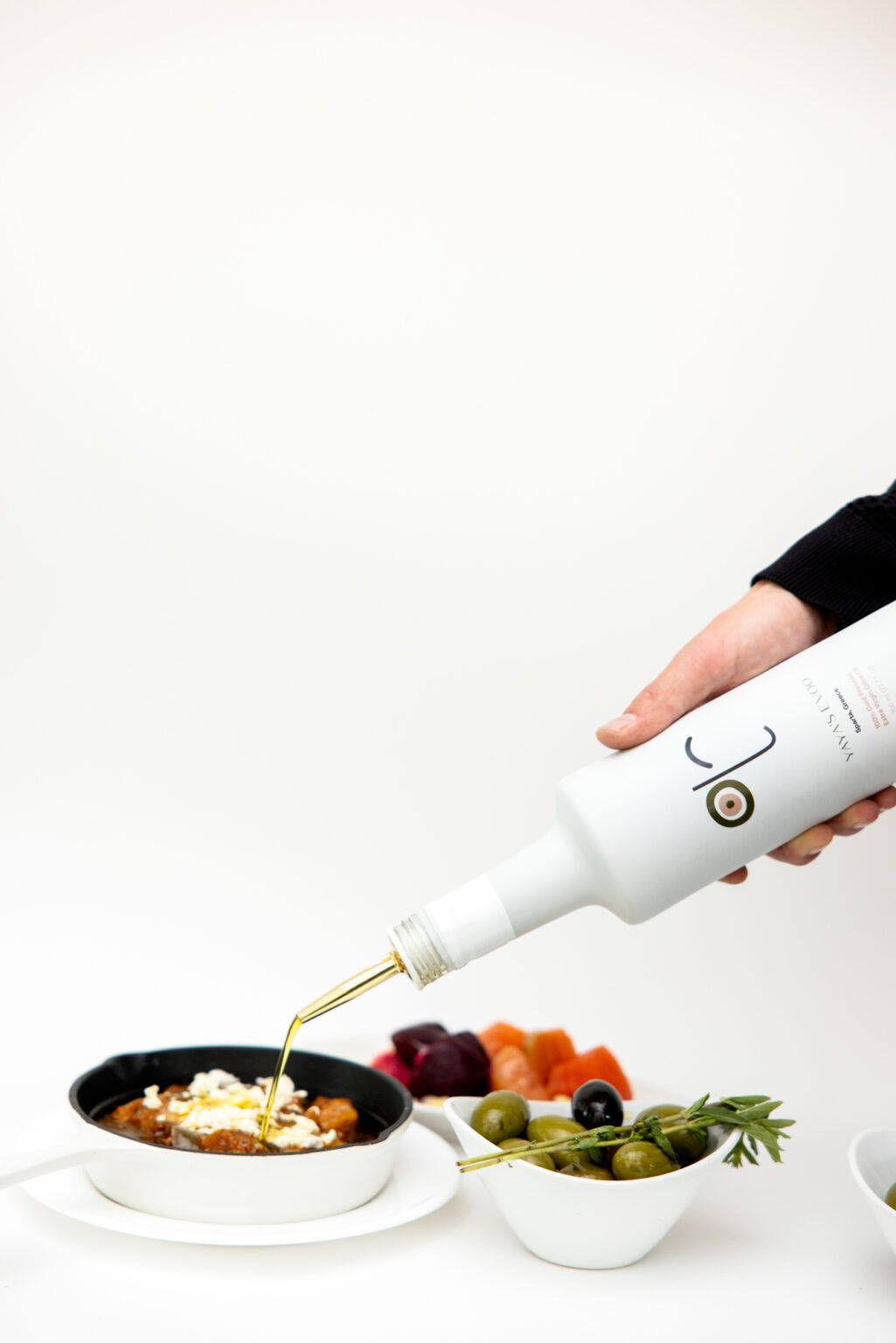 White bottle pours olive oil in a thin stream over food and dishes in a minimalist composition sequence.