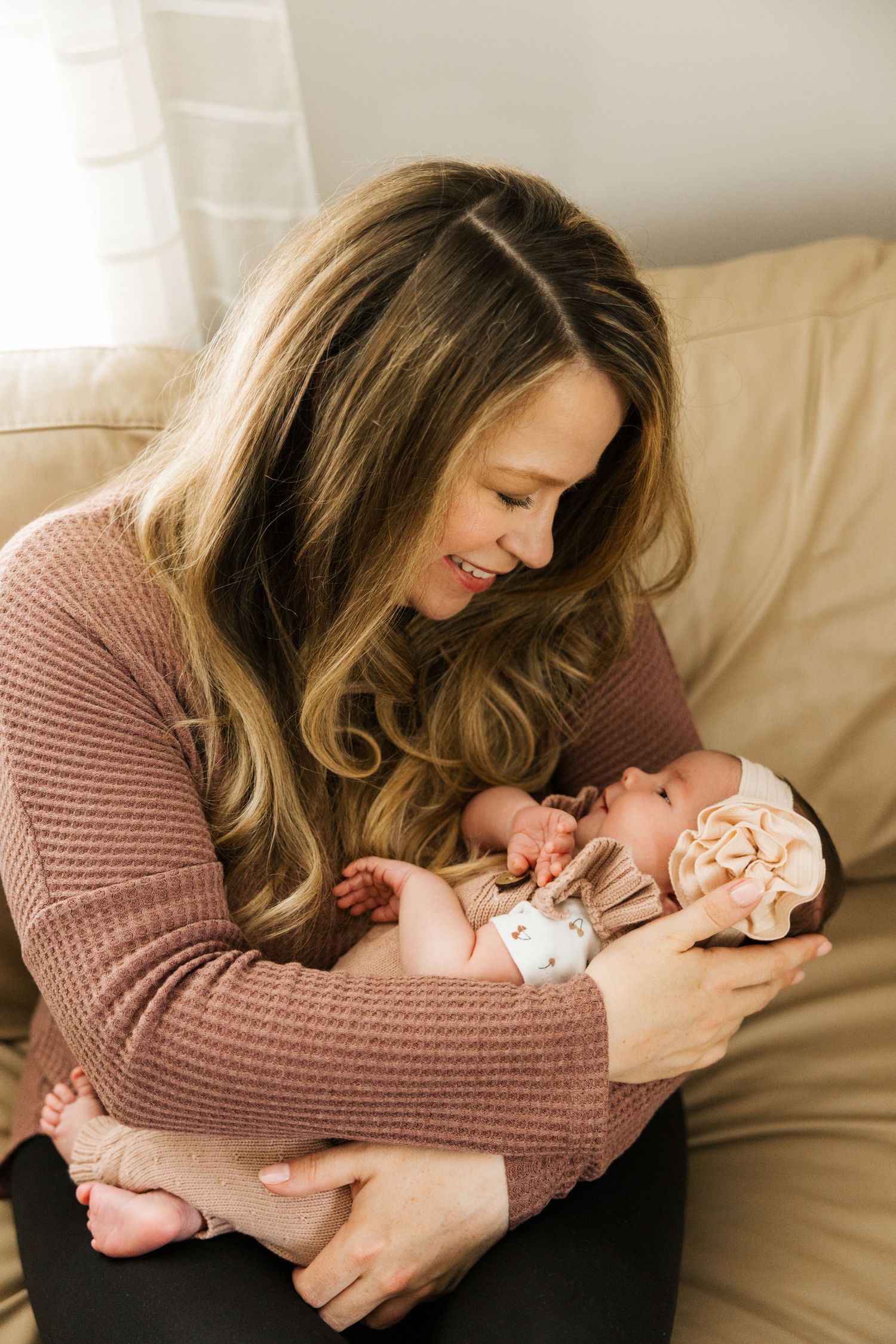 Mother wearing brown sweater cradles and bonds with newborn baby in series of natural light photos.