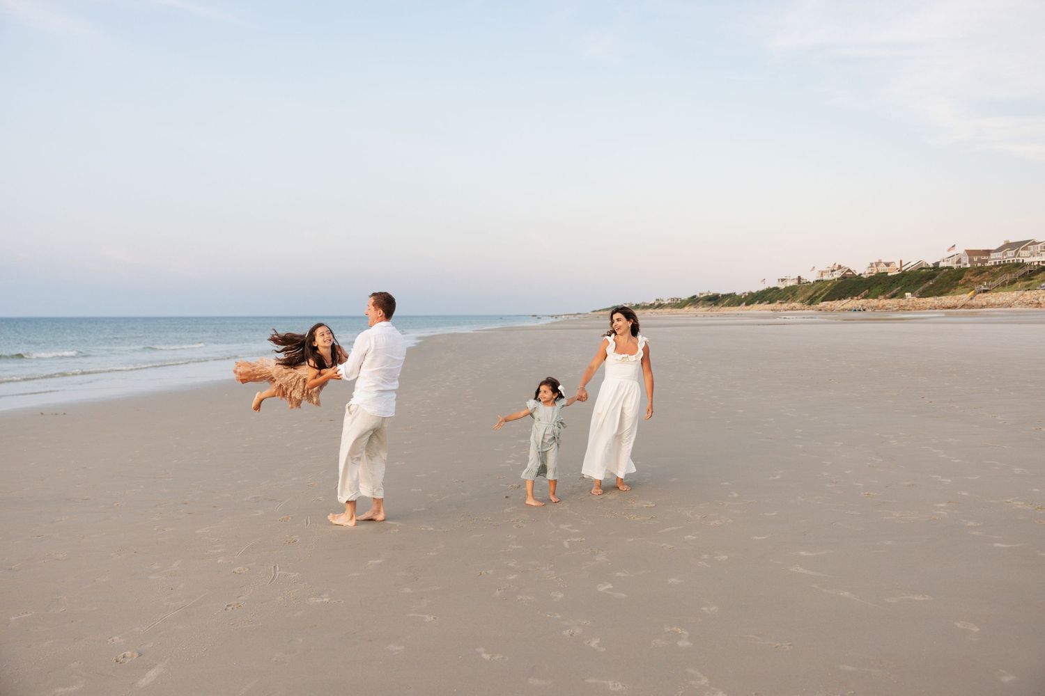 People dressed in white outfits walk along a sandy beach with a serene ocean view during a photo session.