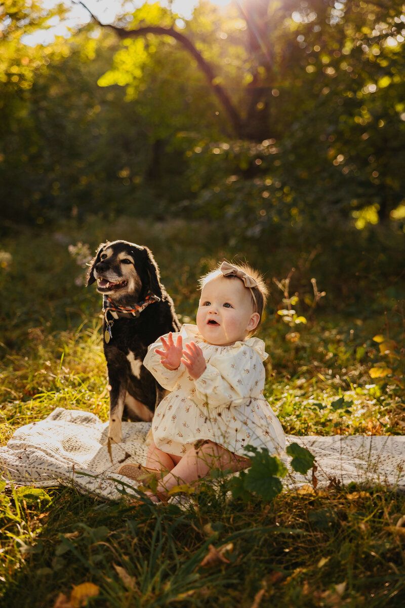 Baby in floral outfit laughing while laying on blanket outdoors during sunset.