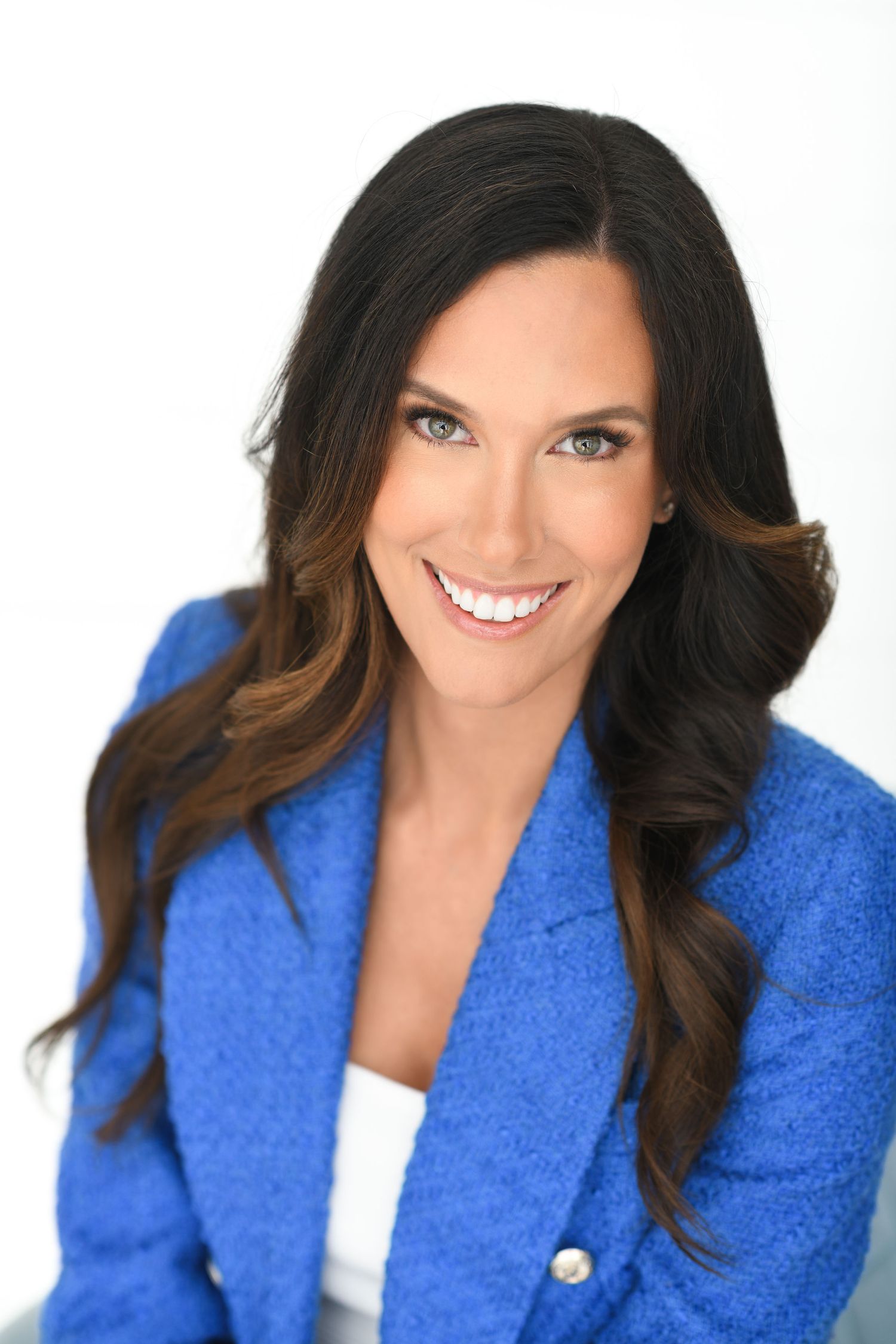 Smiling brunette woman with blue eyes wearing royal blue blazer against white background headshot.