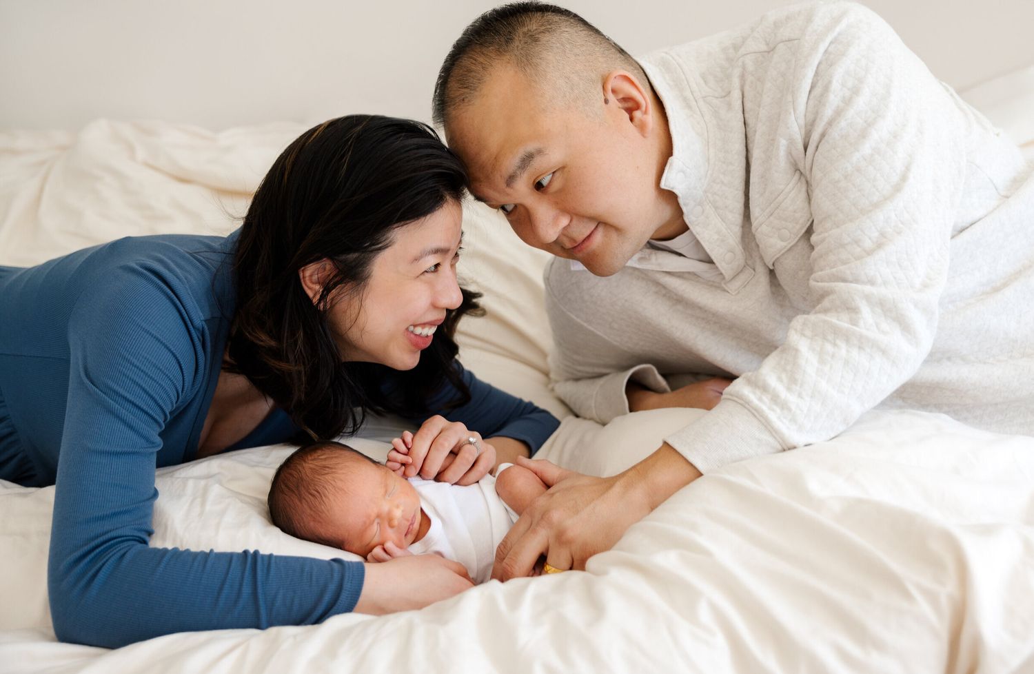 Intimate family moment with sleeping newborn on white bedding.