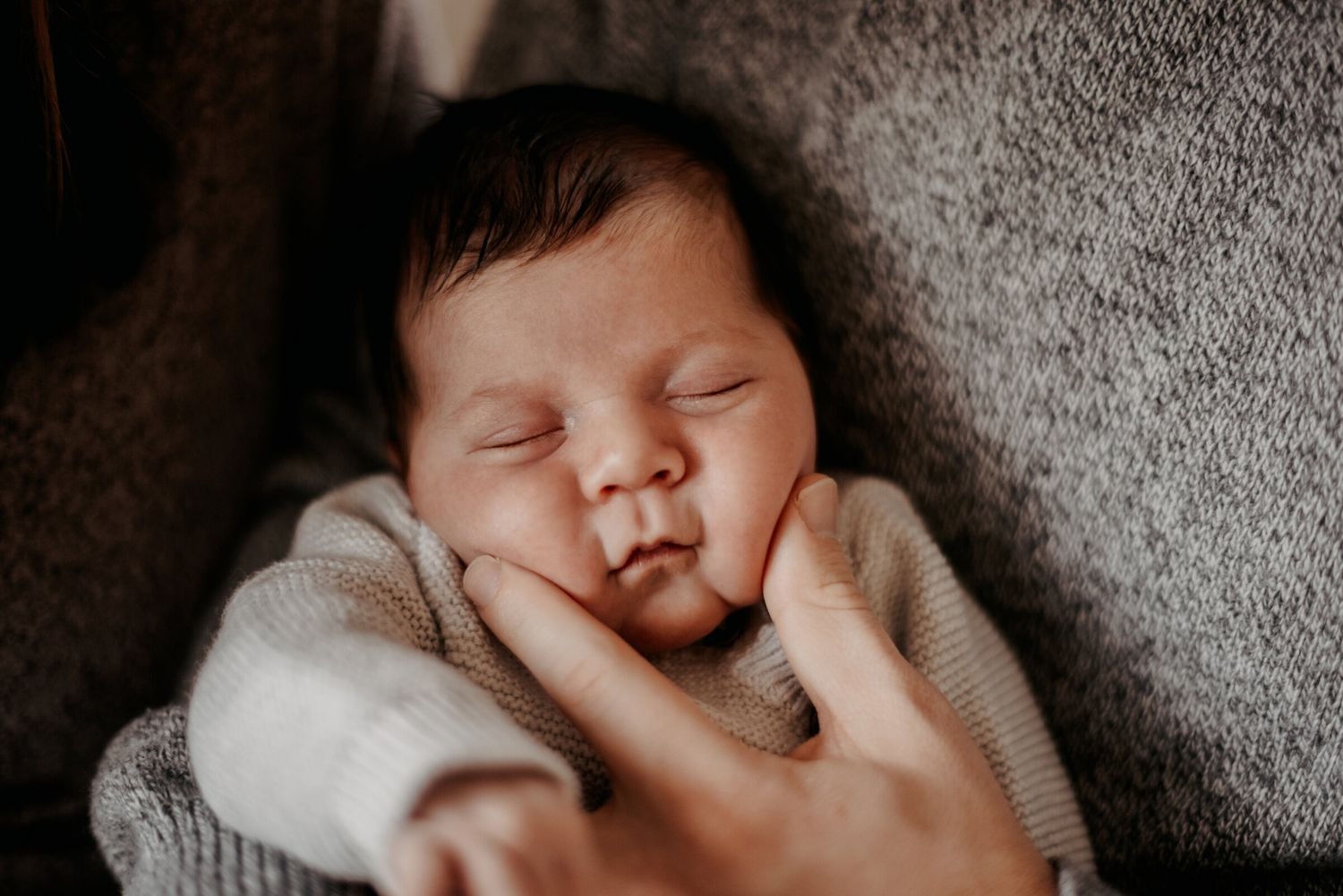 Close-up photo of a sleeping baby lying on soft gray bedding in natural light.