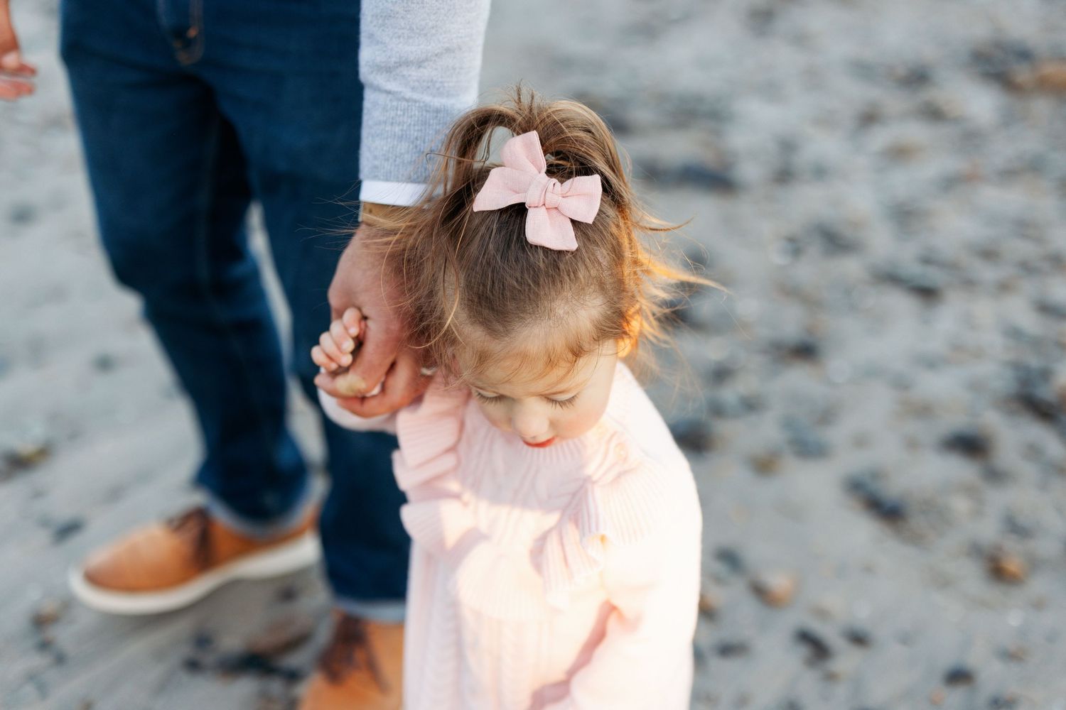 Small child walking with pink bow accessory visible against dark background.