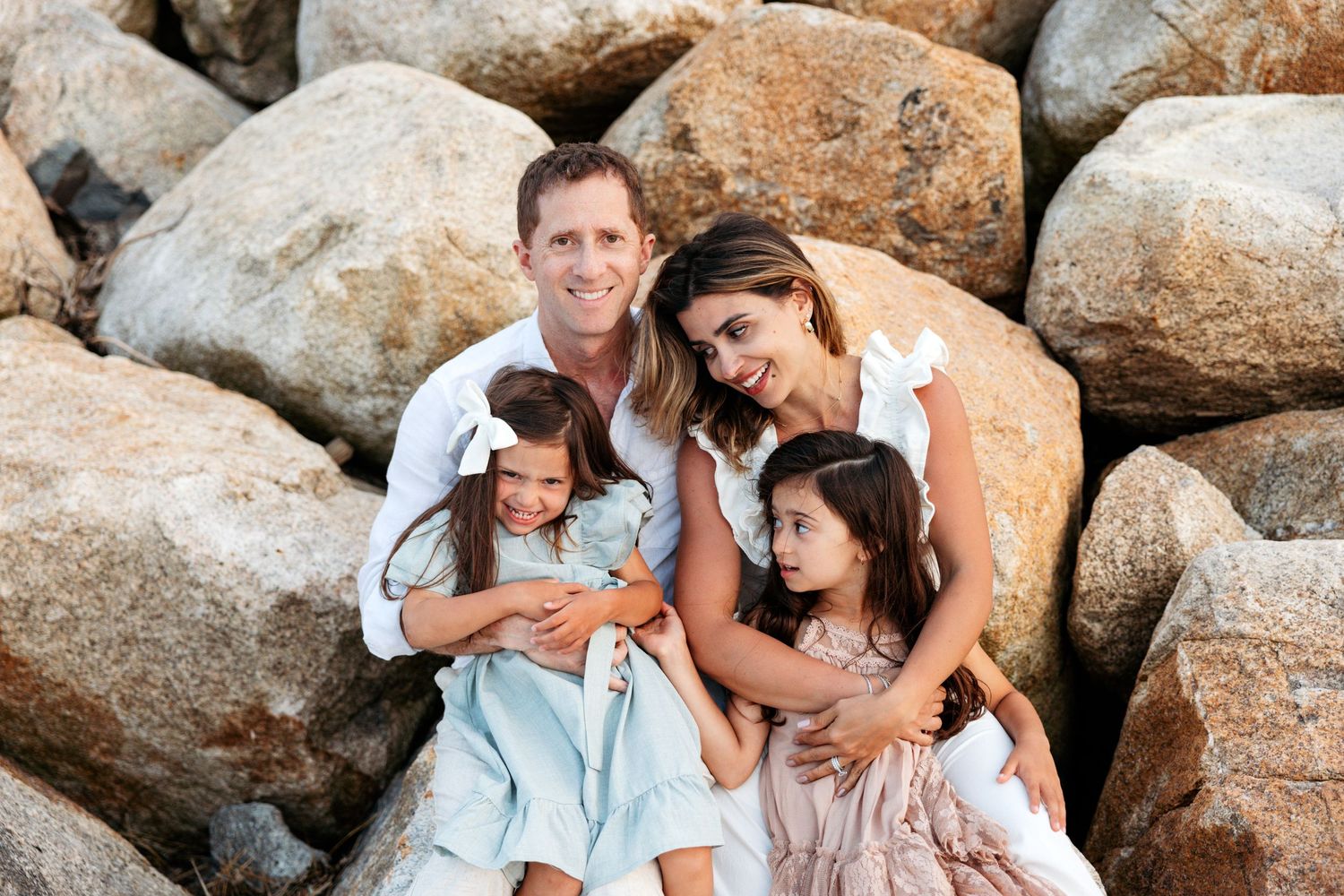 Family portrait series captured on rocky beach terrain showing natural candid interactions.