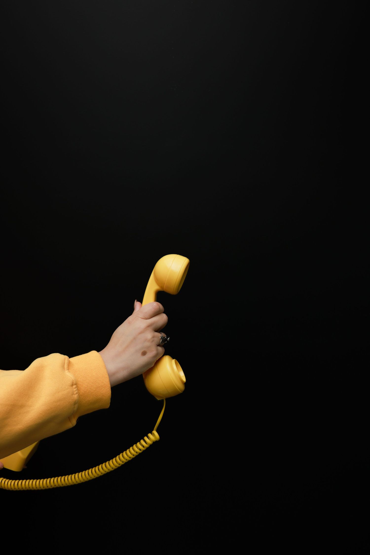 Hand holding yellow vintage telephone receiver against dark background.