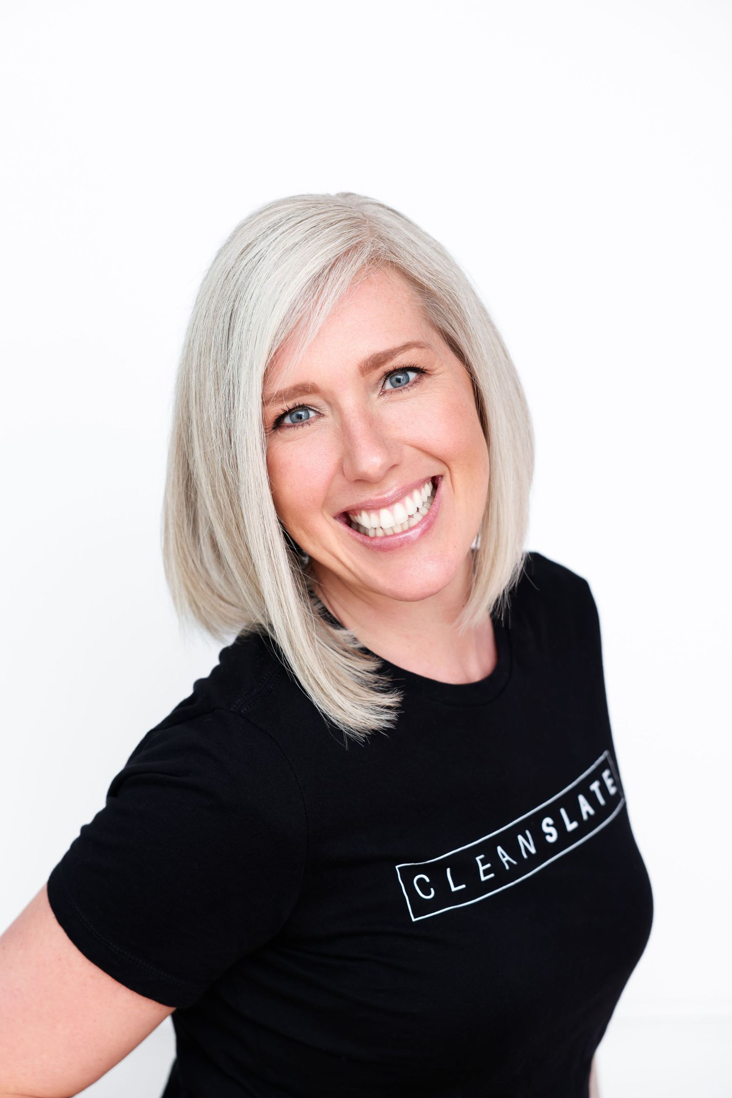 Smiling woman with silver blonde bob wearing a black Clean Slate t-shirt against a white background.