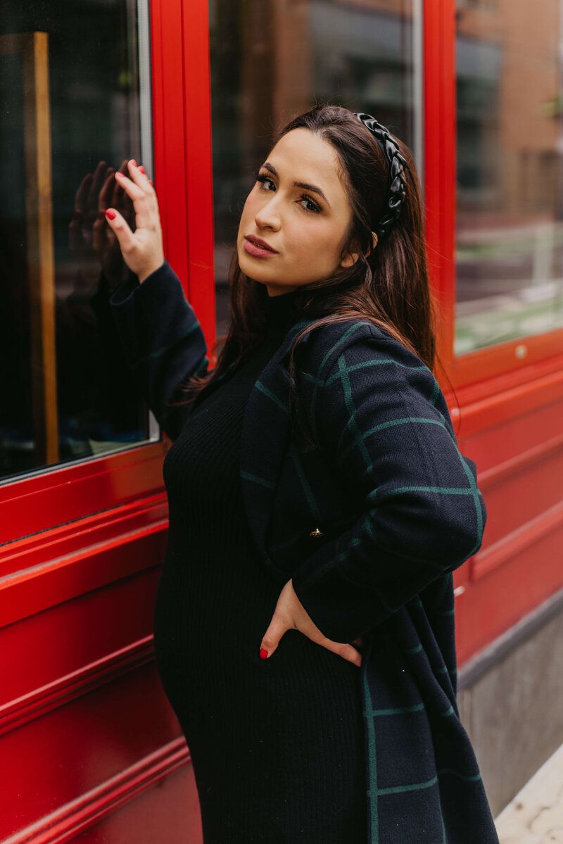 Fashion portrait against vibrant red storefront window with dramatic lighting.