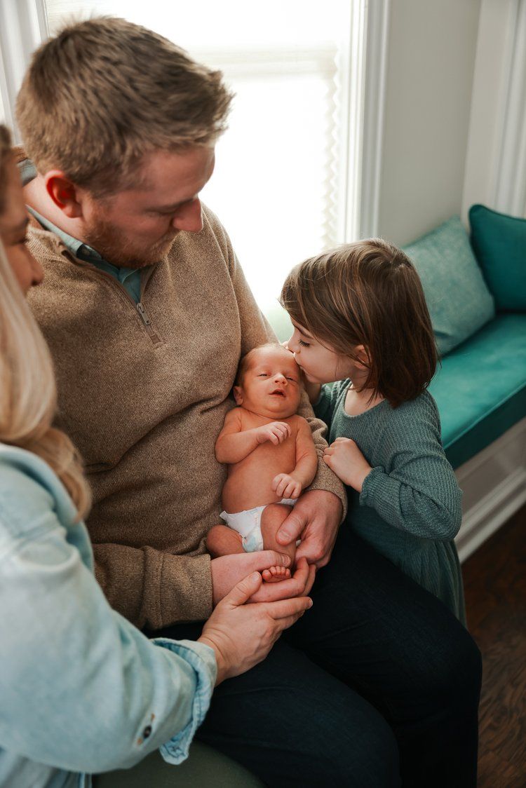 A family shares tender moments together on a couch with a teal cushion in a bright, sunlit room.