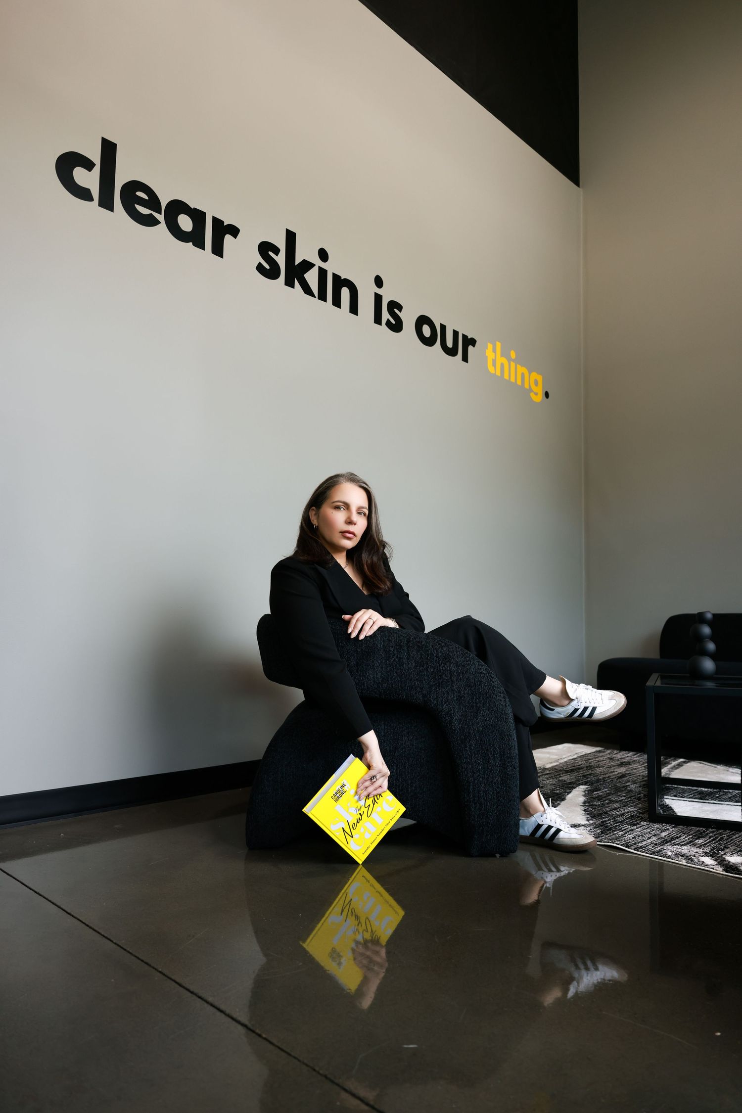 Person wearing black clothes lying on reflective floor next to yellow sign in minimalist space.