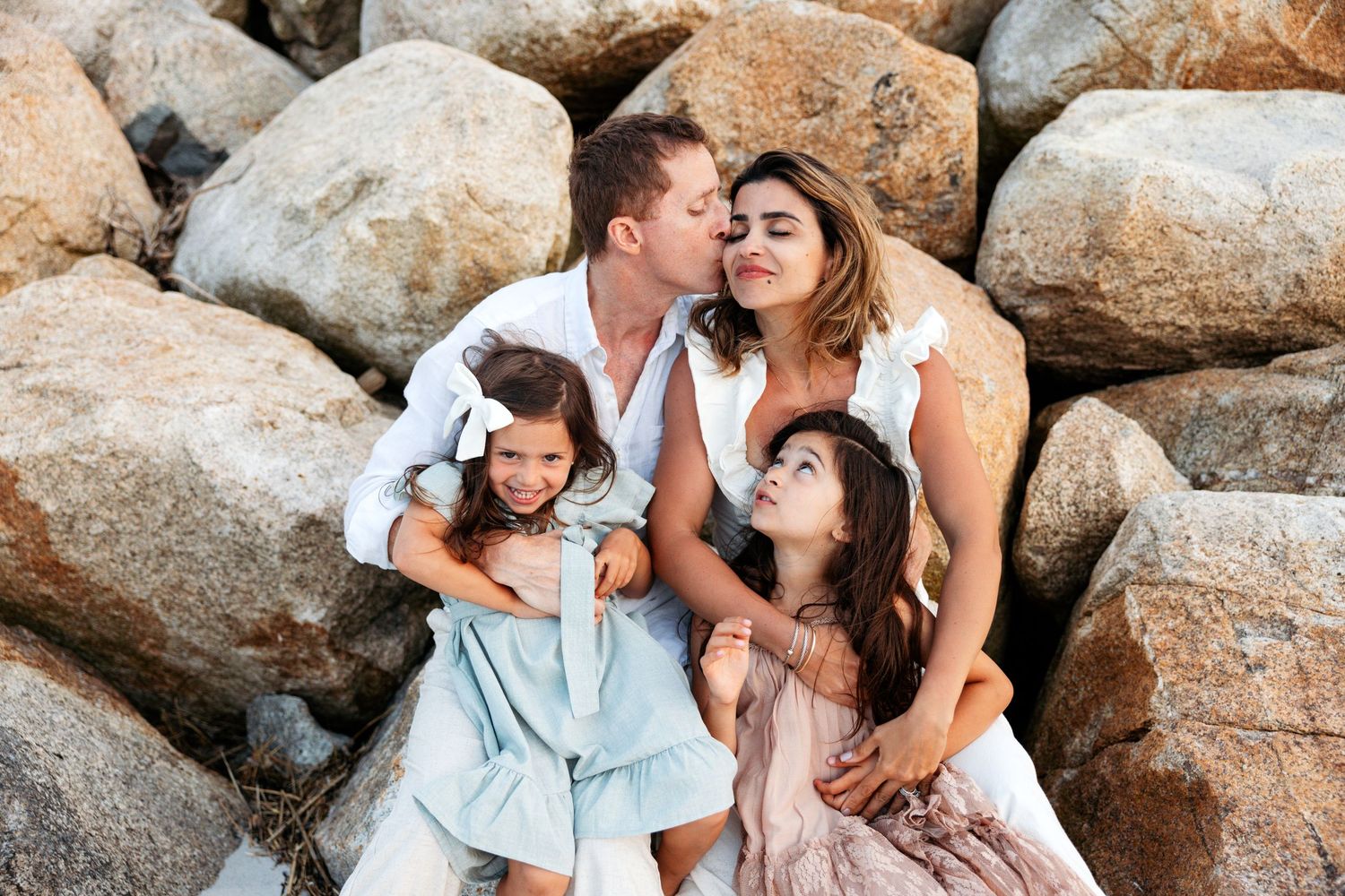 Romantic coastal photoshoot with couples posed among large rocks at the beach.