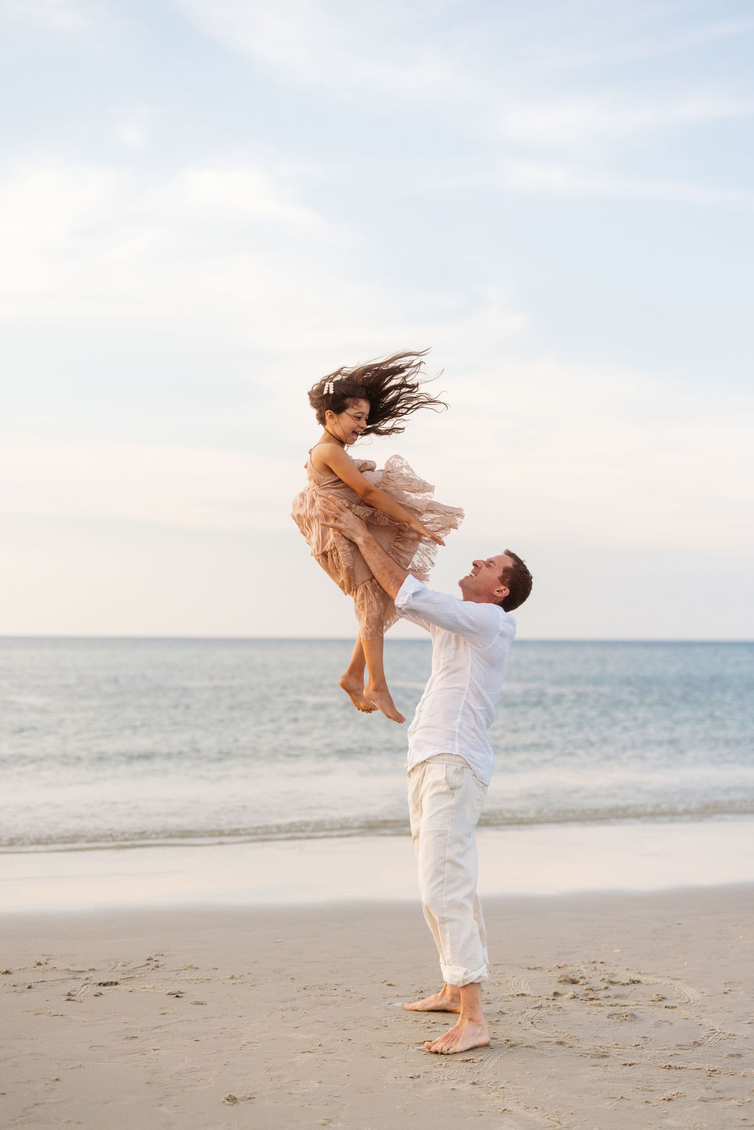 Father lifts child high in the air while playing on a beach at sunset.