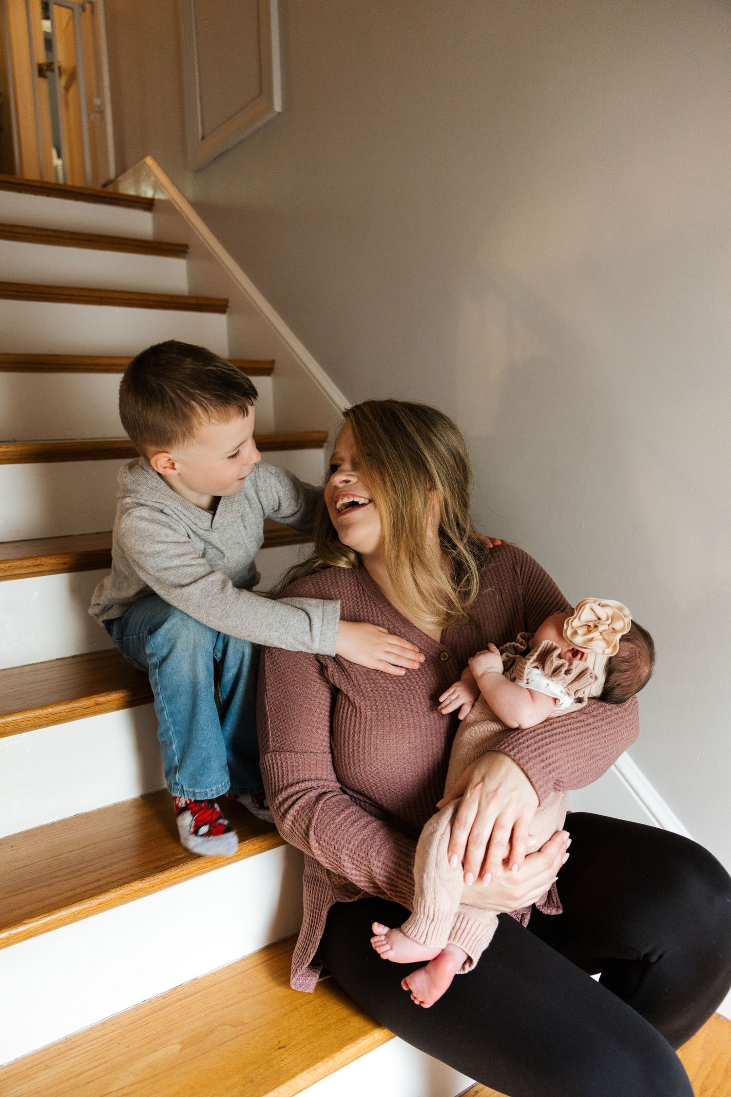 Candid family moment on wooden stairs shows playful interaction in warm natural lighting.