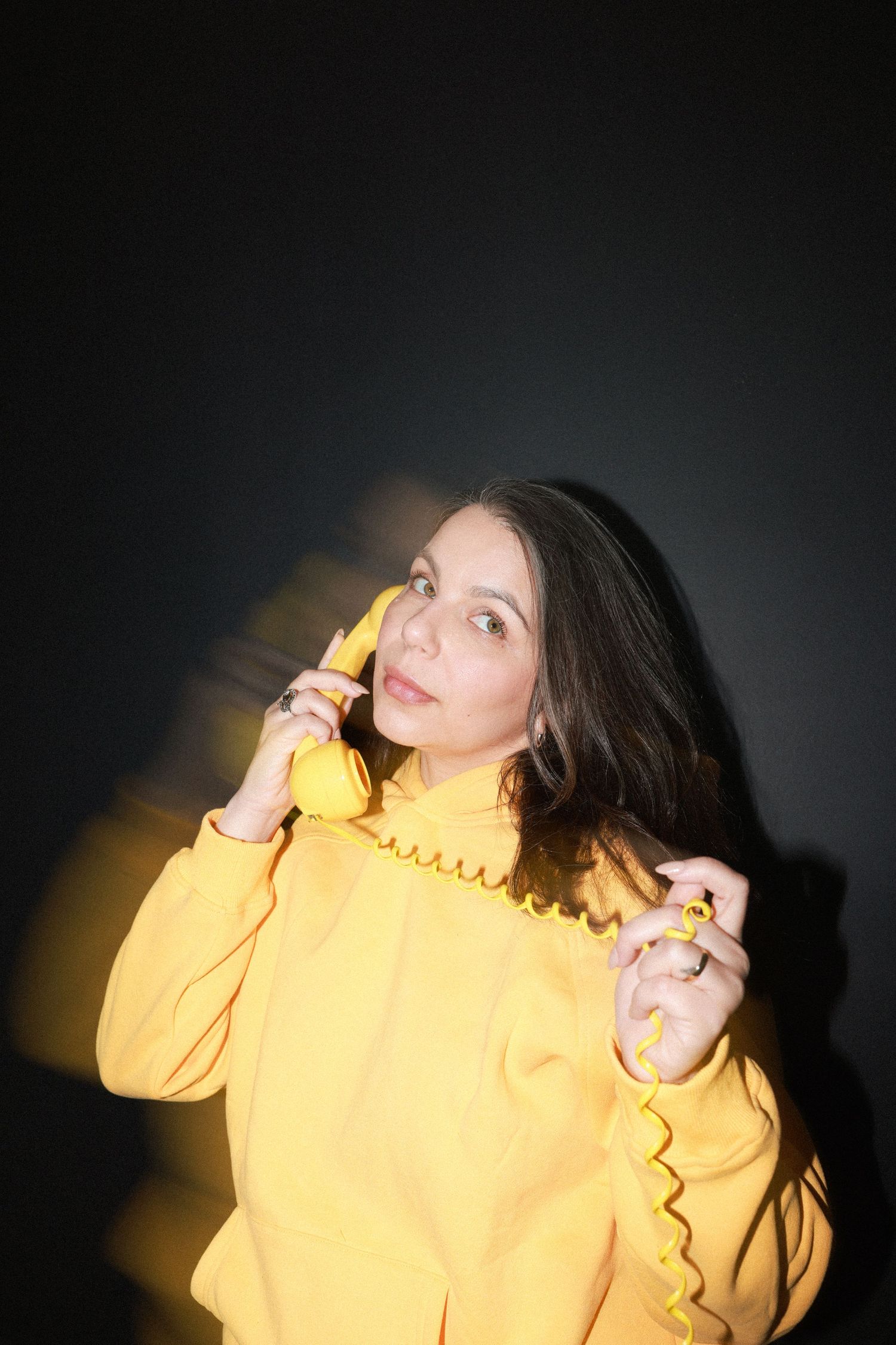 Person in bright yellow sweater poses dramatically against dark background with corded telephone.