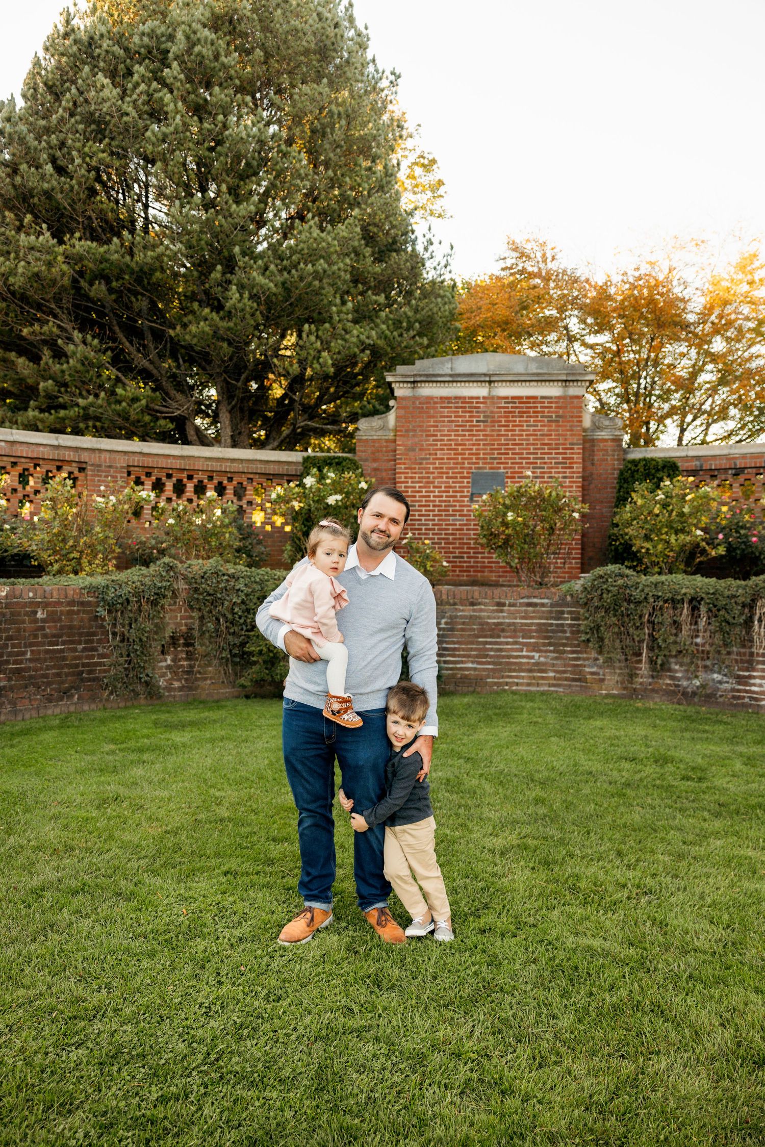 Family playing together on a grassy lawn with brick walls and fall trees in the background.