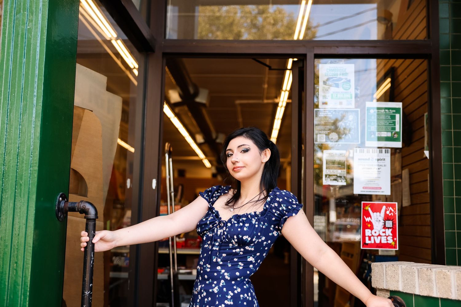 Person in a navy polka dot dress poses dramatically in a doorway with green trim and fluorescent lighting.