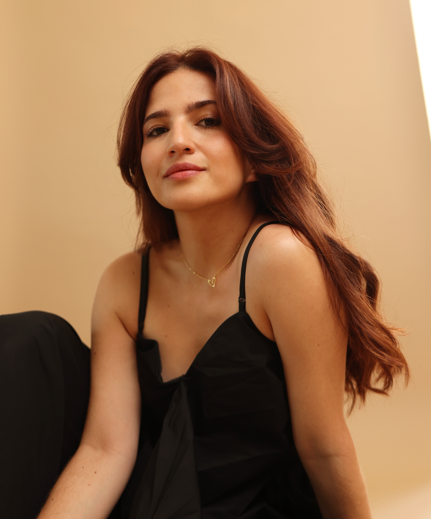 Person with dark hair in black outfit poses seductively in a candid photo series against neutral background.