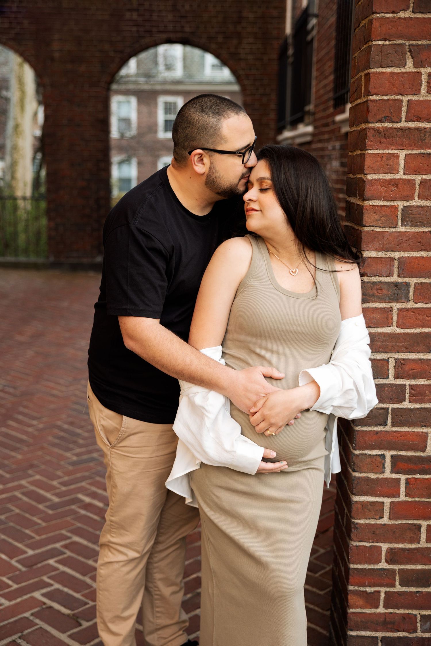 Intimate maternity photos against brick wall showing couple embracing.