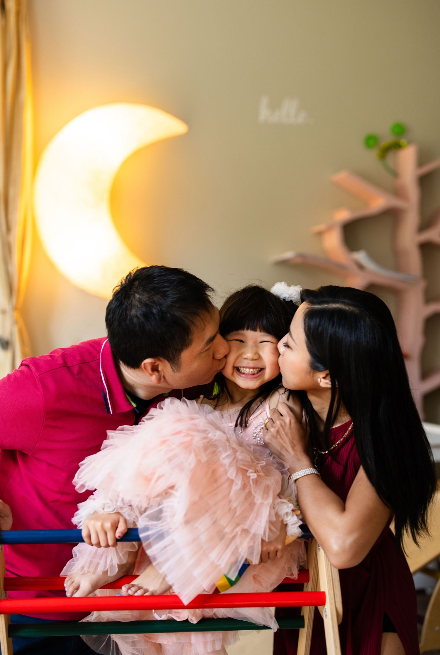 A family shares loving kisses while sitting together on a couch in matching pink and magenta outfits.