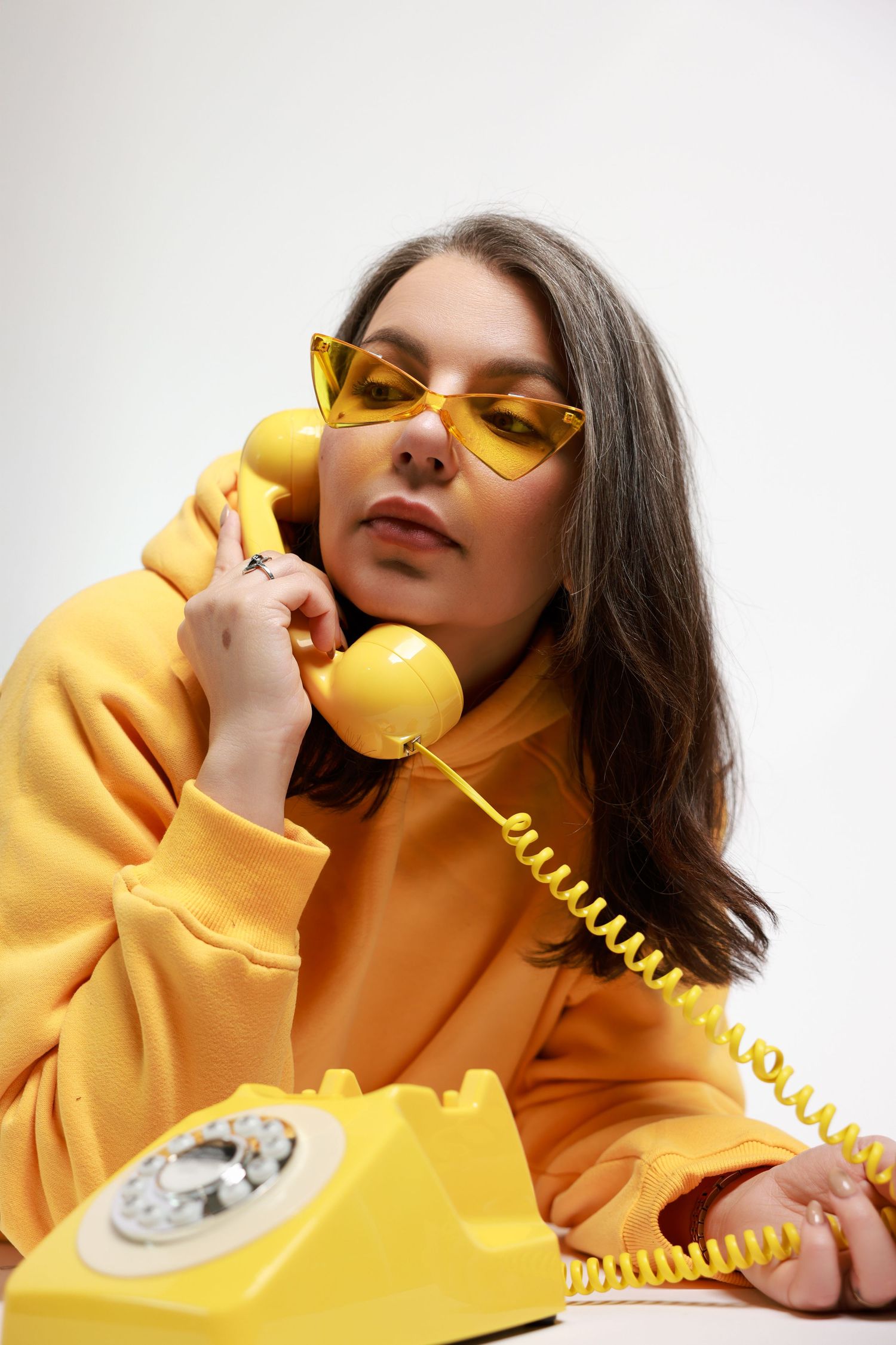 Creative photoshoot with vintage yellow telephone and matching yellow outfit against white background.