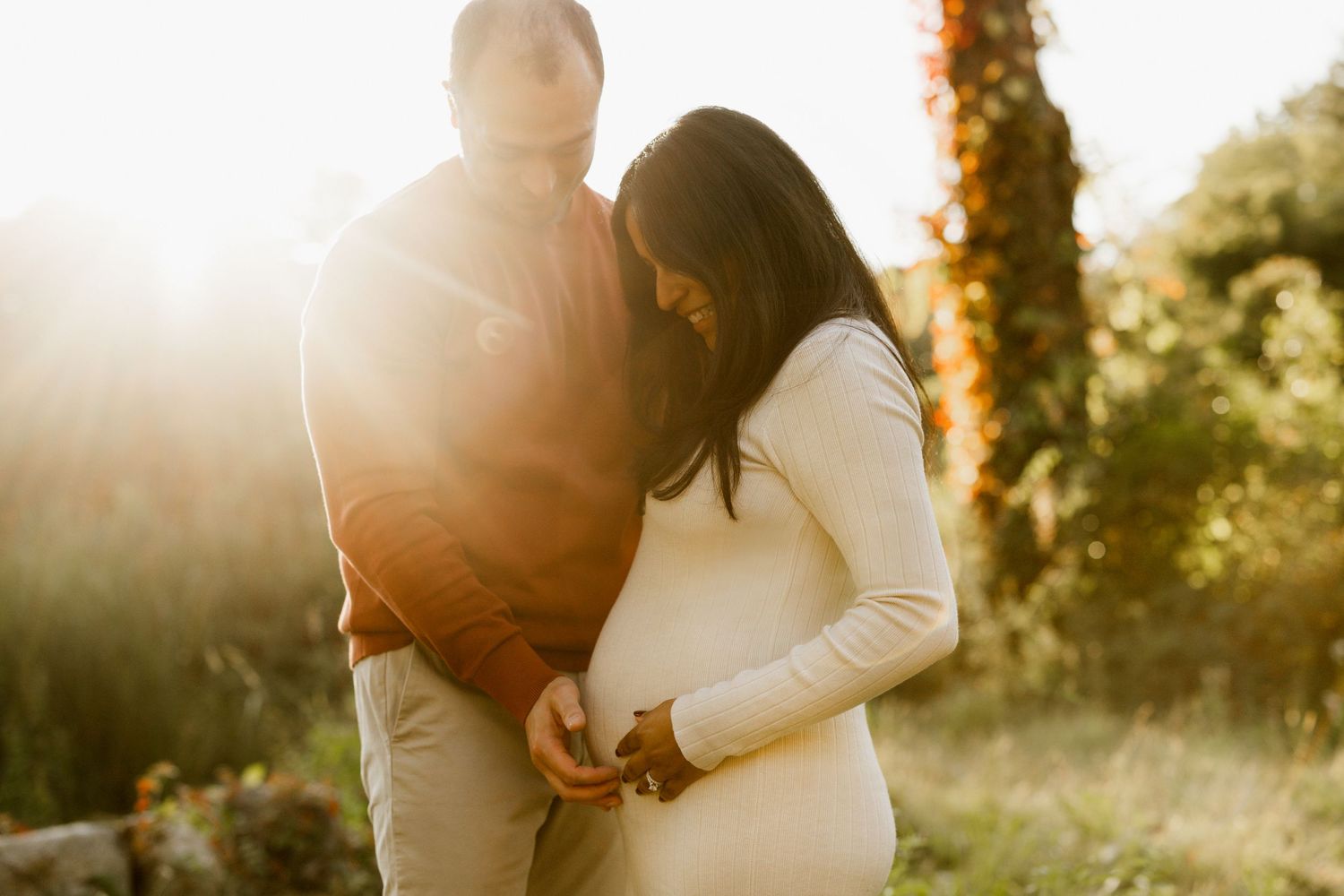 Romantic maternity photo session in a sunlit field during golden hour at sunset.