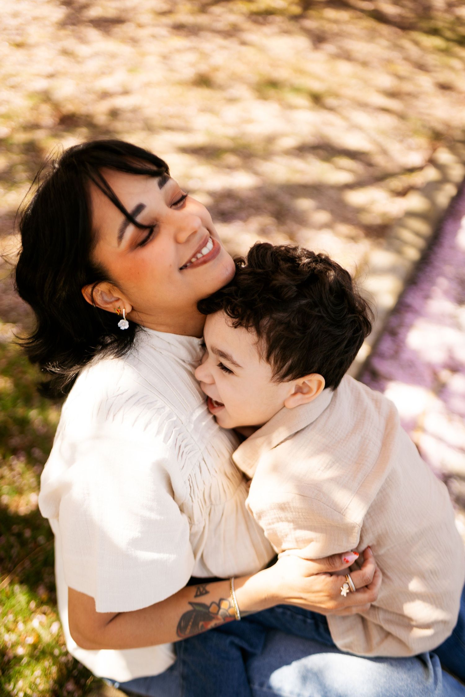 Mother embracing and showing affection to young child in outdoor setting with natural light filtering through trees.