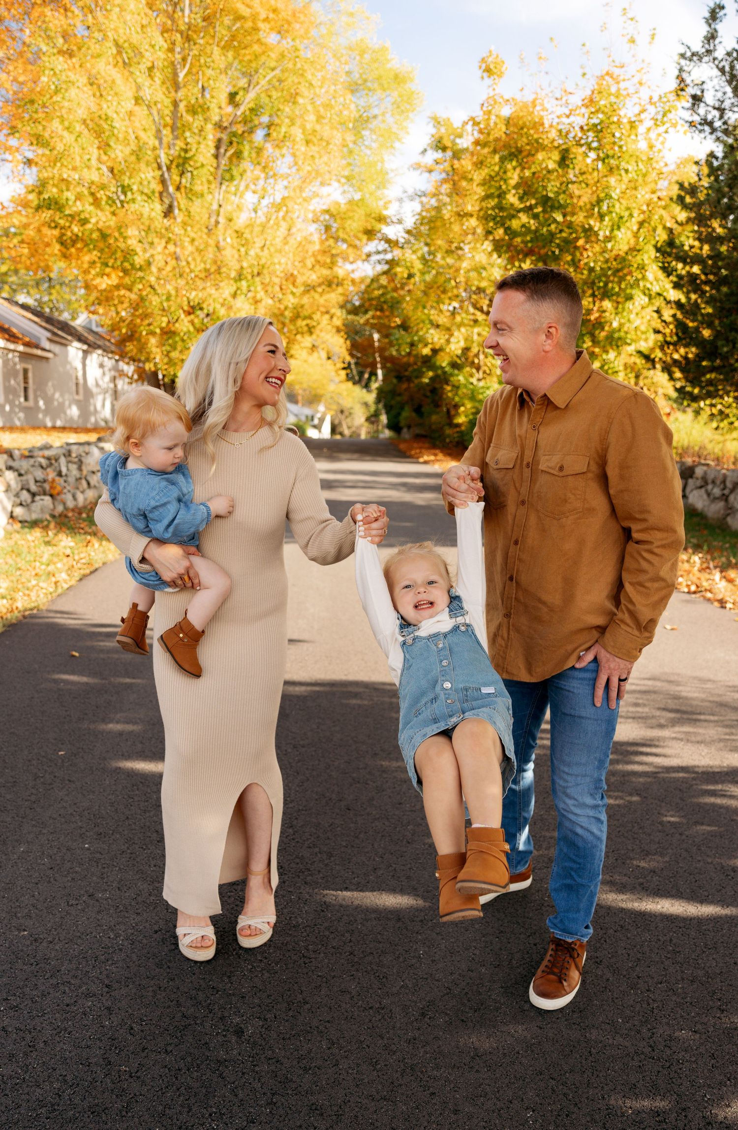 Family members share joyful moments together under vibrant fall foliage on a residential street.