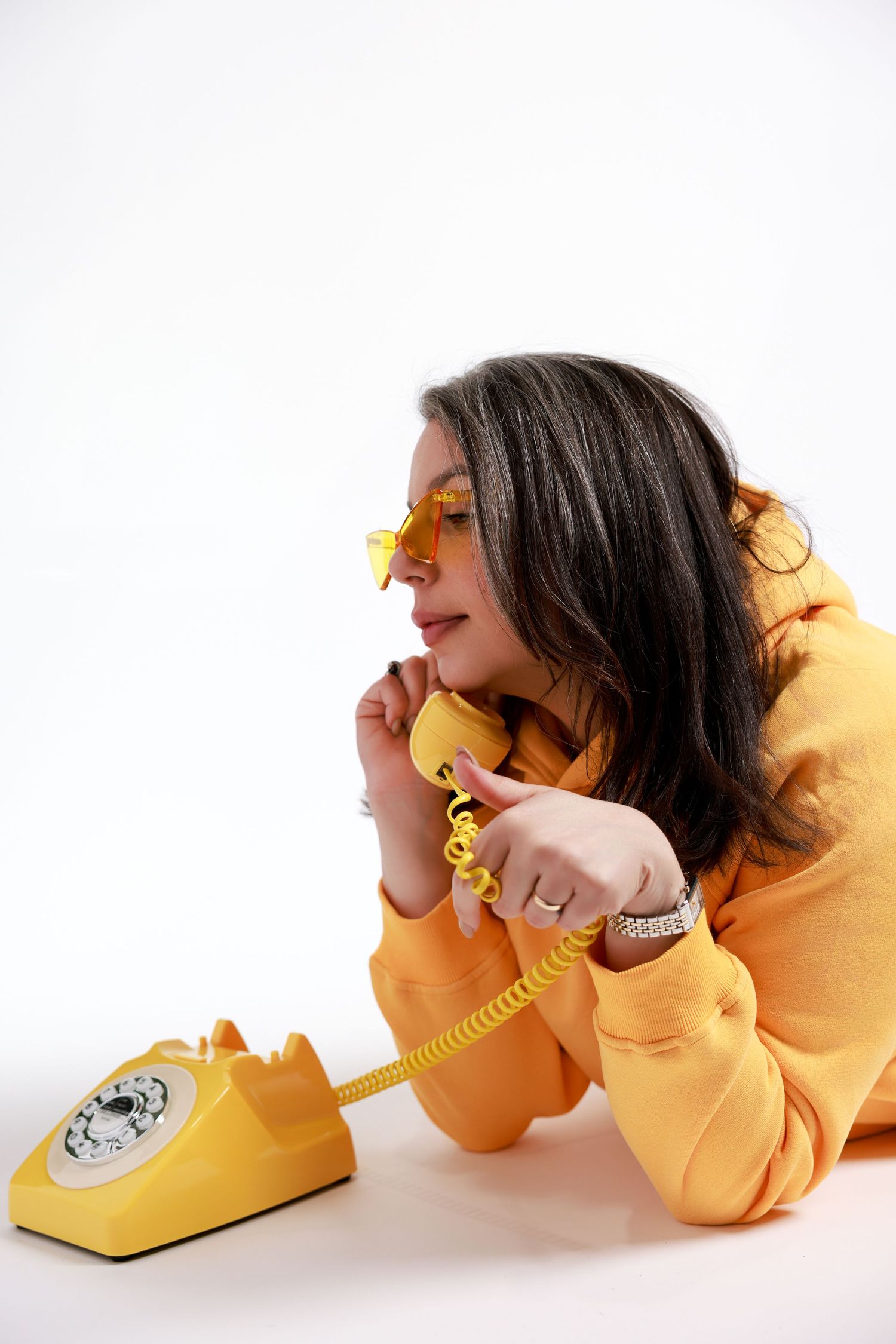 Person in yellow sweater talking on vintage yellow rotary telephone against white backdrop.