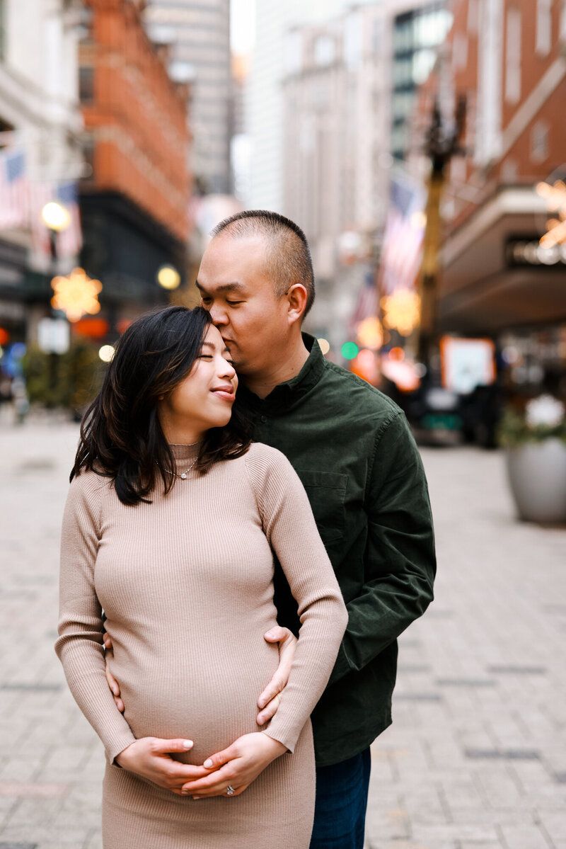 Intimate moment between couple on city street with person in green sweater and beige dress.