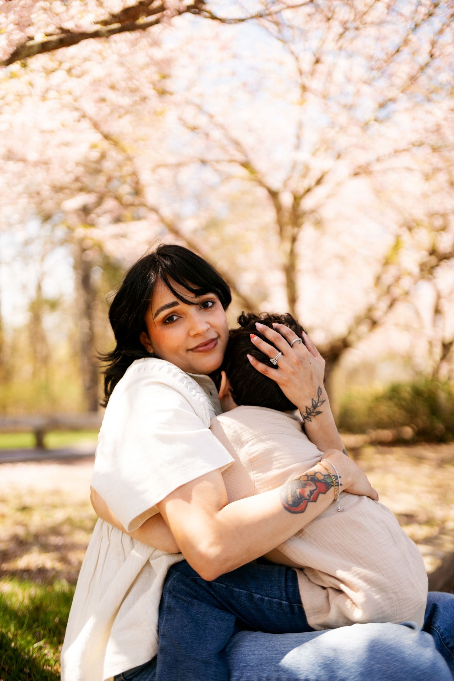 A tender moment captured beneath blooming cherry blossoms as figures cuddle close together in a spring setting.