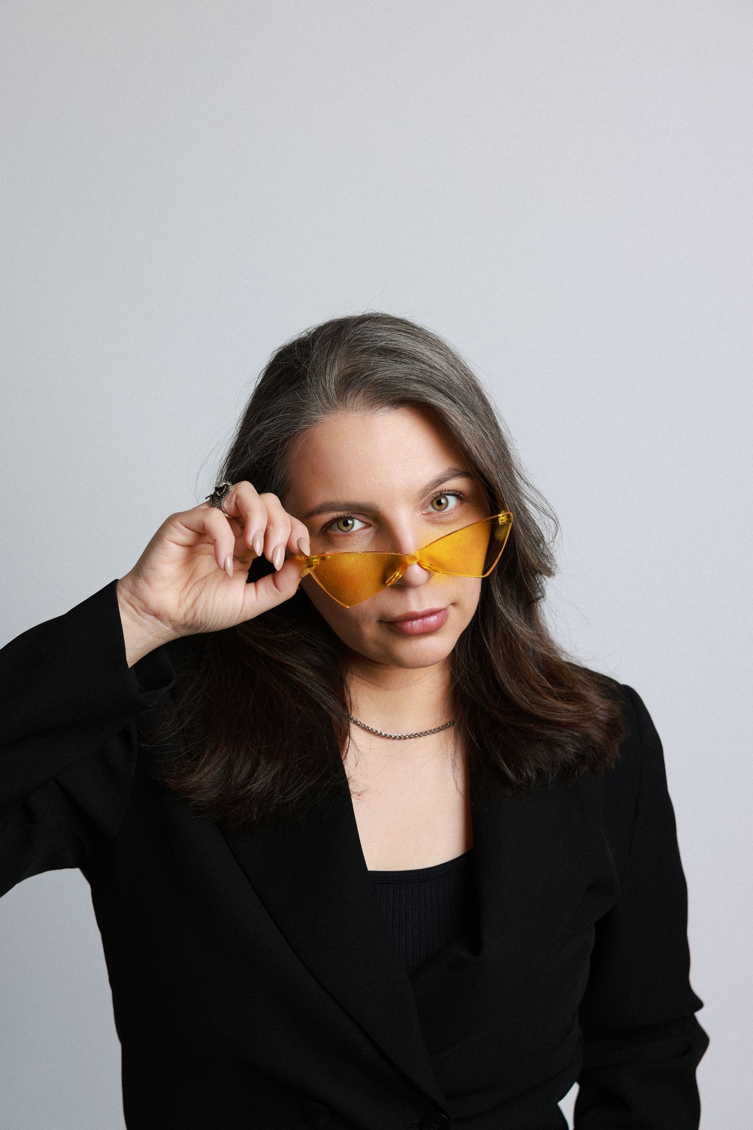 Four sequential fashion shots show a model in black blazer wearing orange-tinted sunglasses against a white backdrop.