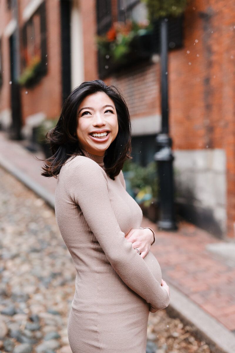 Person in beige sweater dress smiling joyfully on a historic cobblestone street.