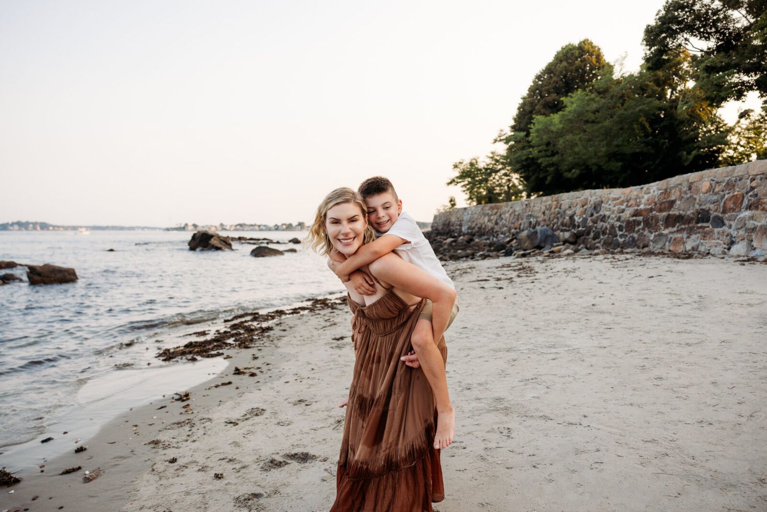 Two people walk along a sandy ocean beach during golden hour with cliffs in the background.