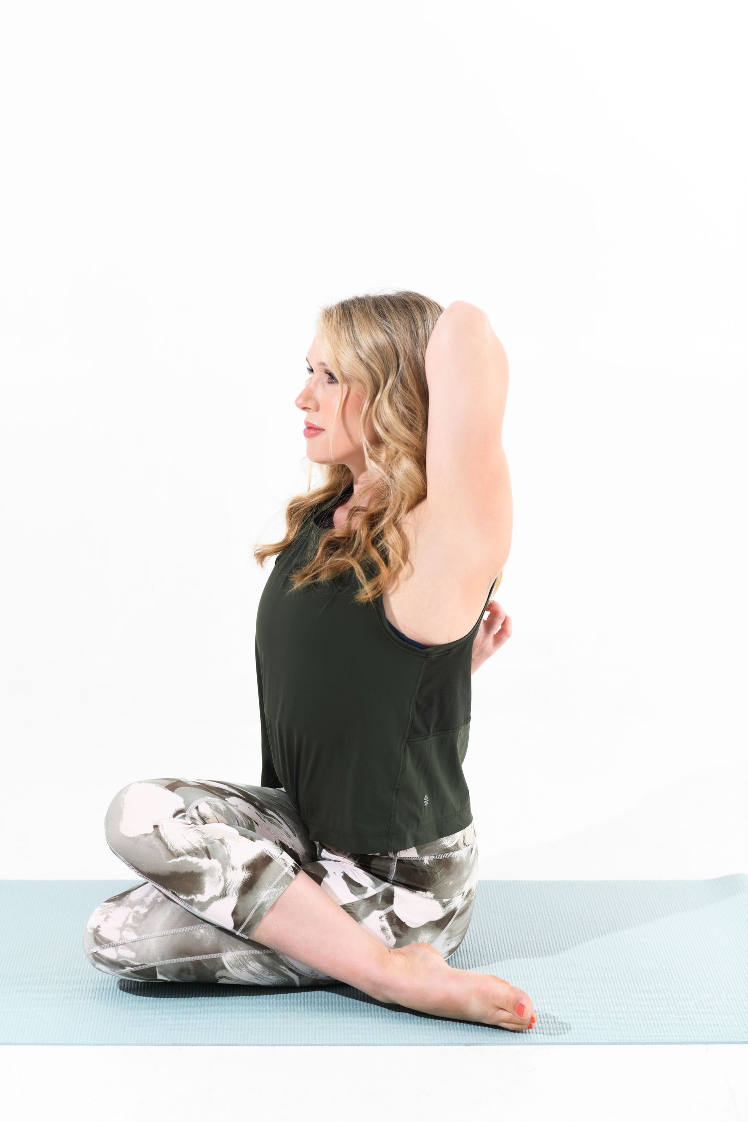 Blonde woman in black top and printed leggings doing seated yoga stretch on blue mat.