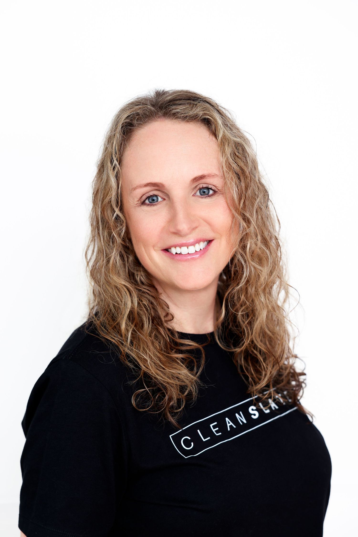 Smiling woman with curly blonde hair wearing a black Clean Slate shirt against a white background.