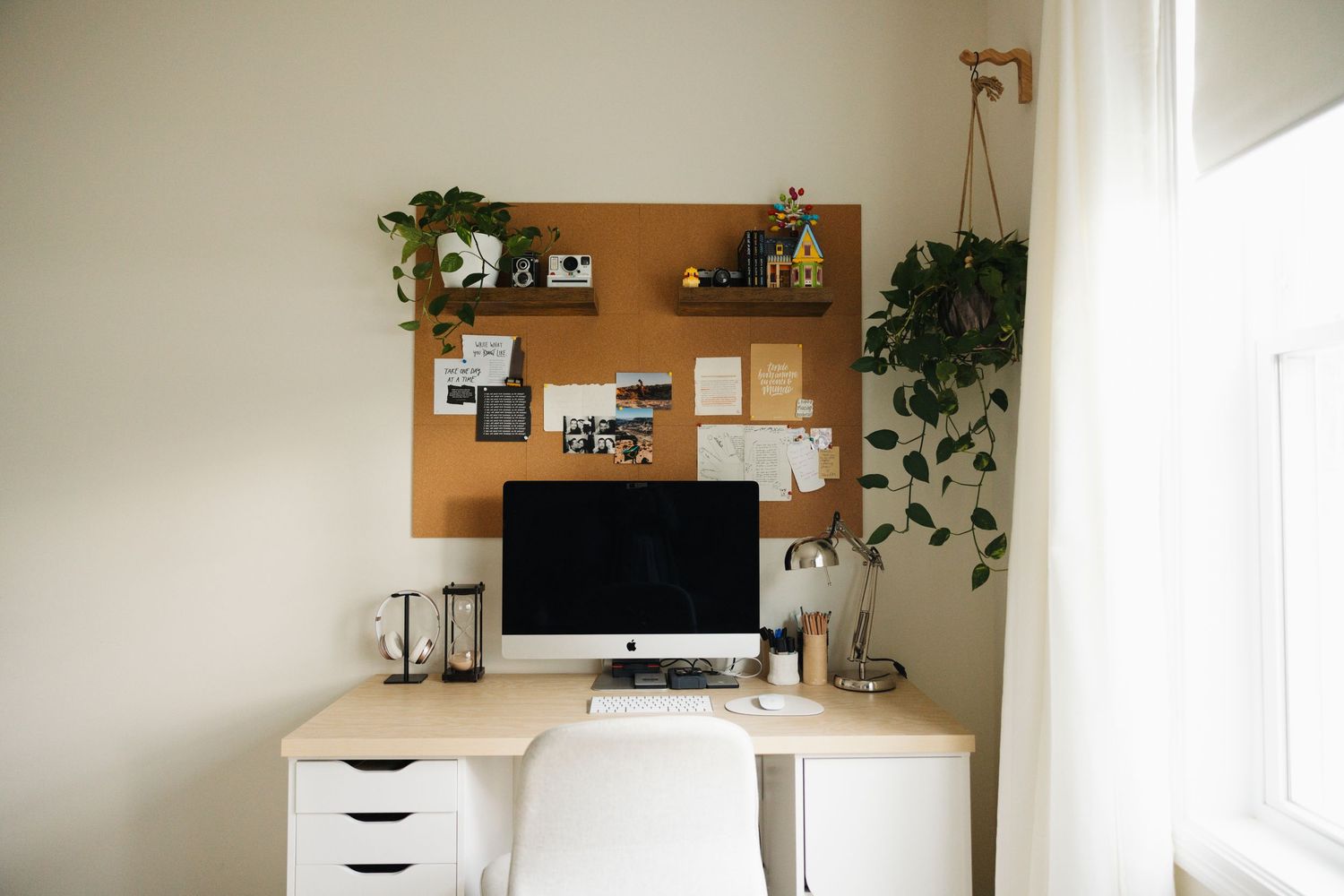 Modern minimalist bedroom interior with white walls, hanging plants, and natural light from large window.