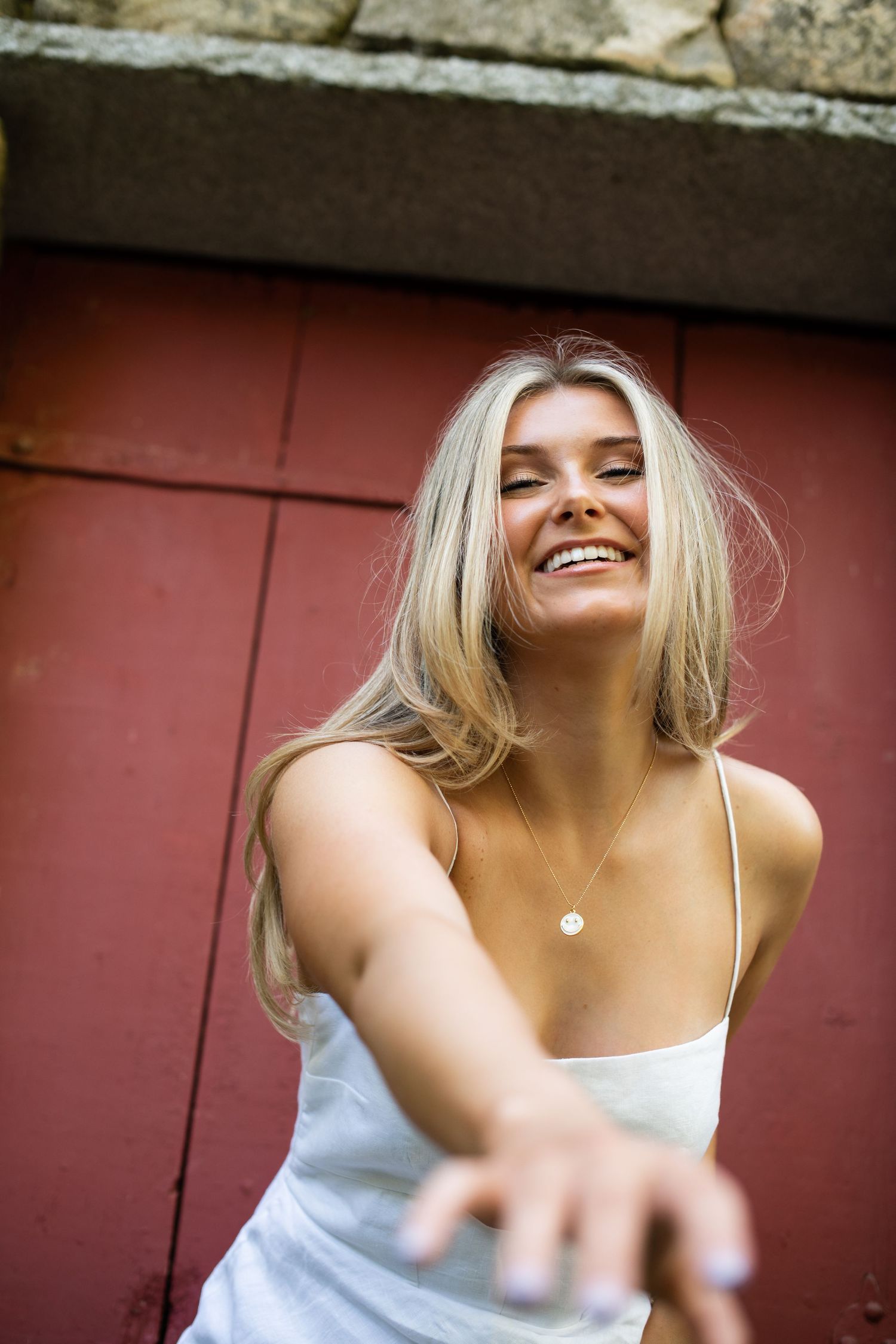 Young woman in white tank top smiles joyfully against red wooden wall background in natural light.