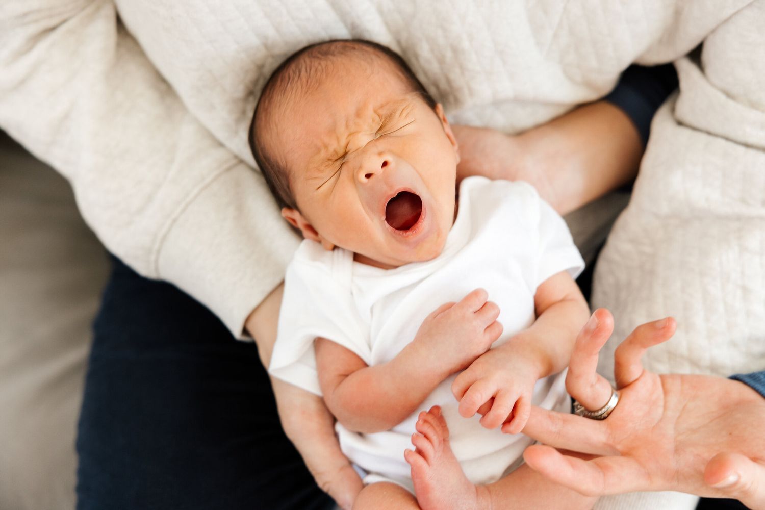 Sleeping newborn baby yawning while wearing white onesie.