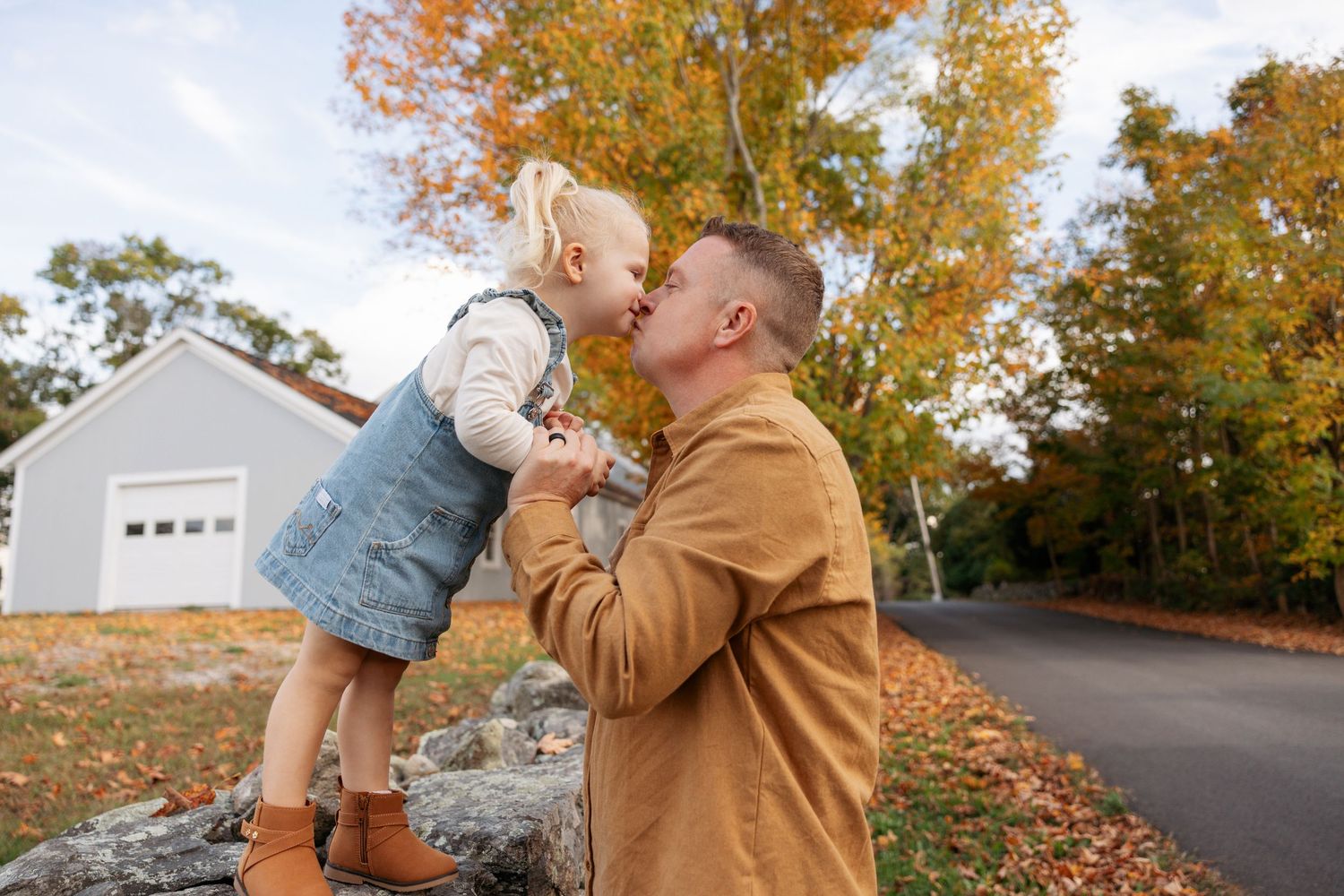 A couple embraces on a fall day with golden leaves and sunshine in the background.