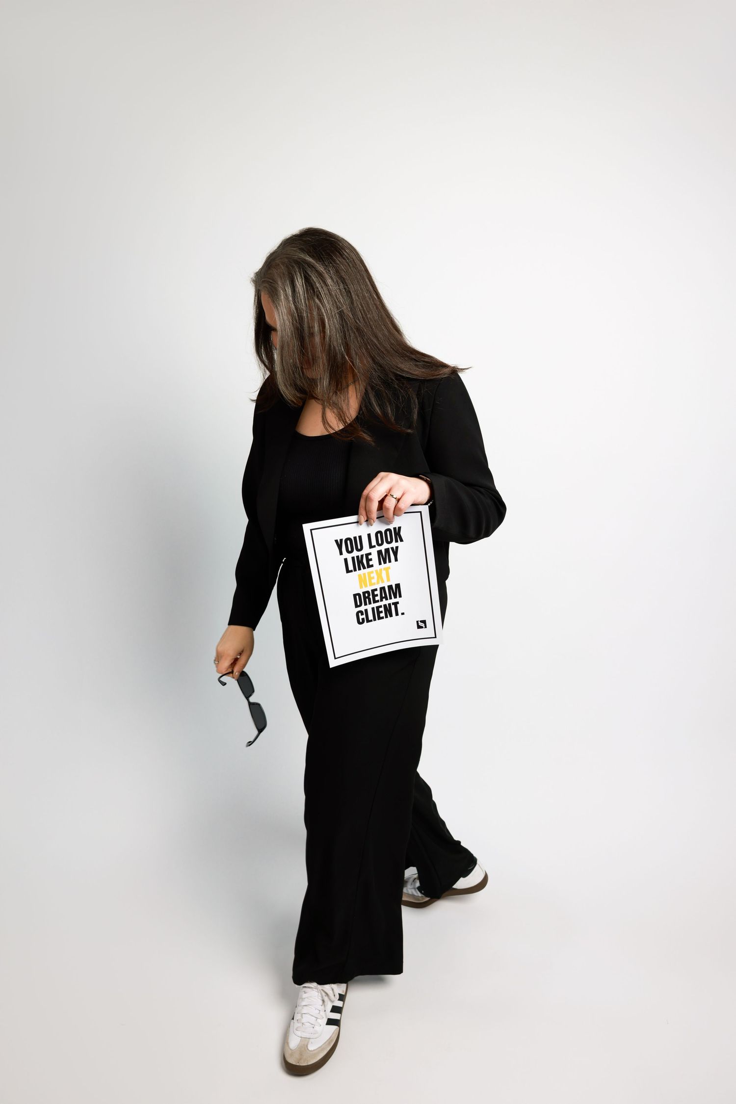 Person wearing black clothing holds up a text card while posing casually on white background.