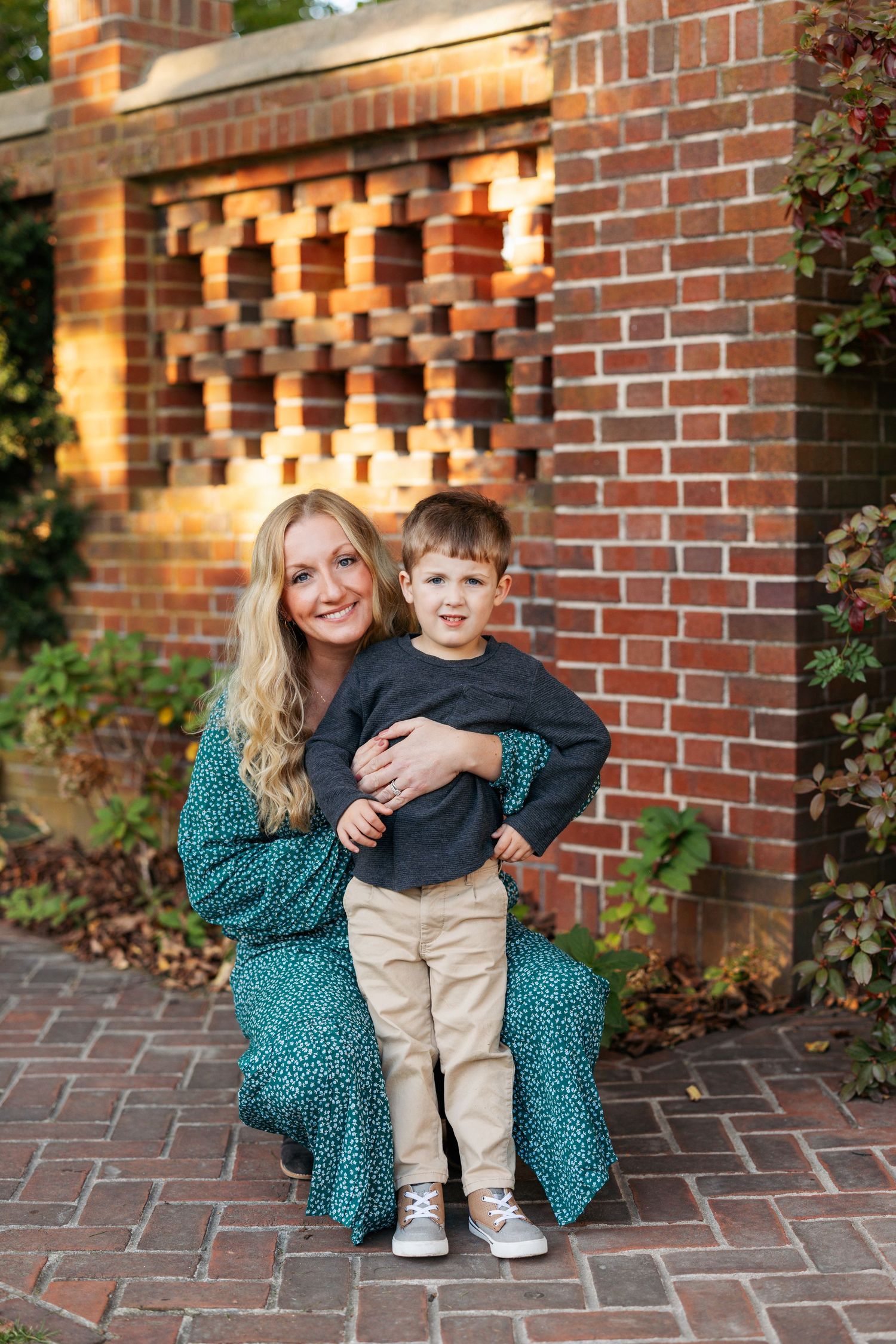 Mother and child sitting together by a brick wall with warm sunset lighting.