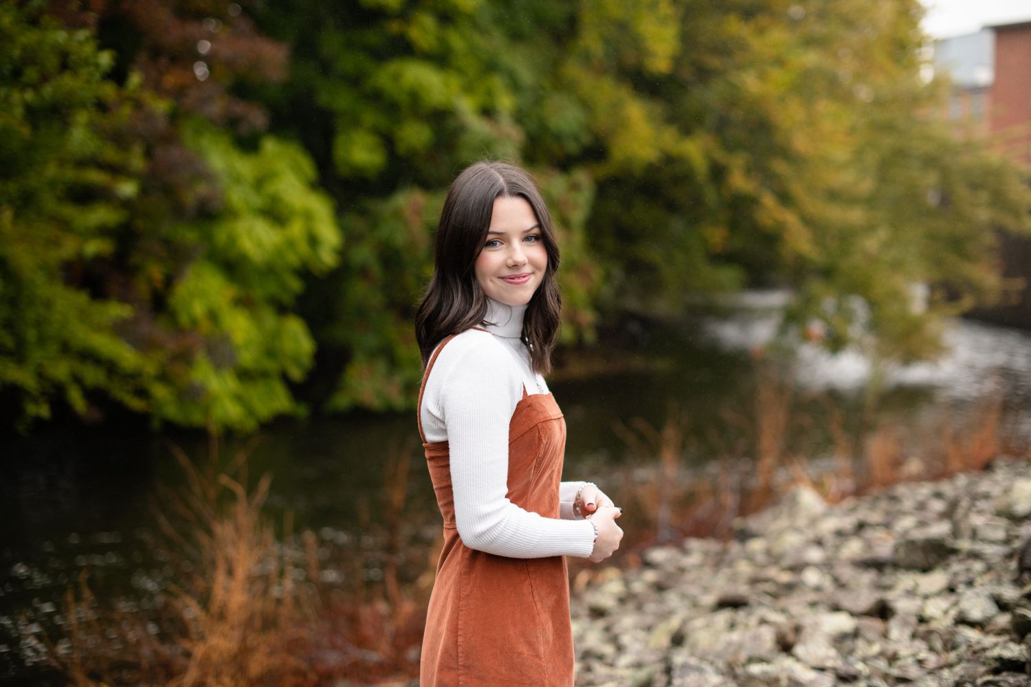 Outdoor portrait session in autumn featuring a brown dress against a natural backdrop with trees and rocks.