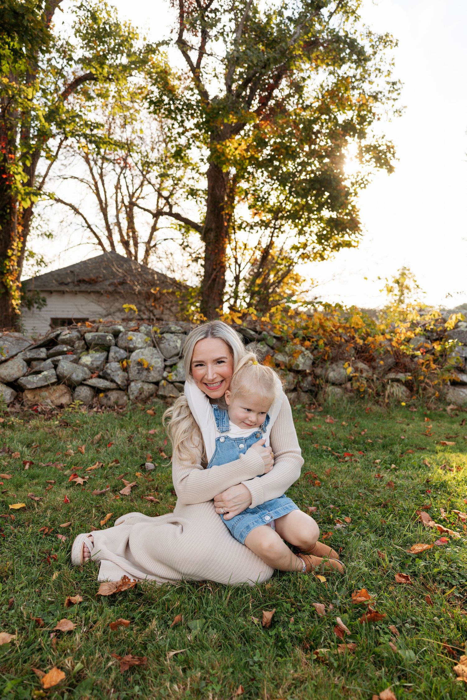 Candid interactions between caregiver and child on grass surrounded by fall foliage and stone wall.